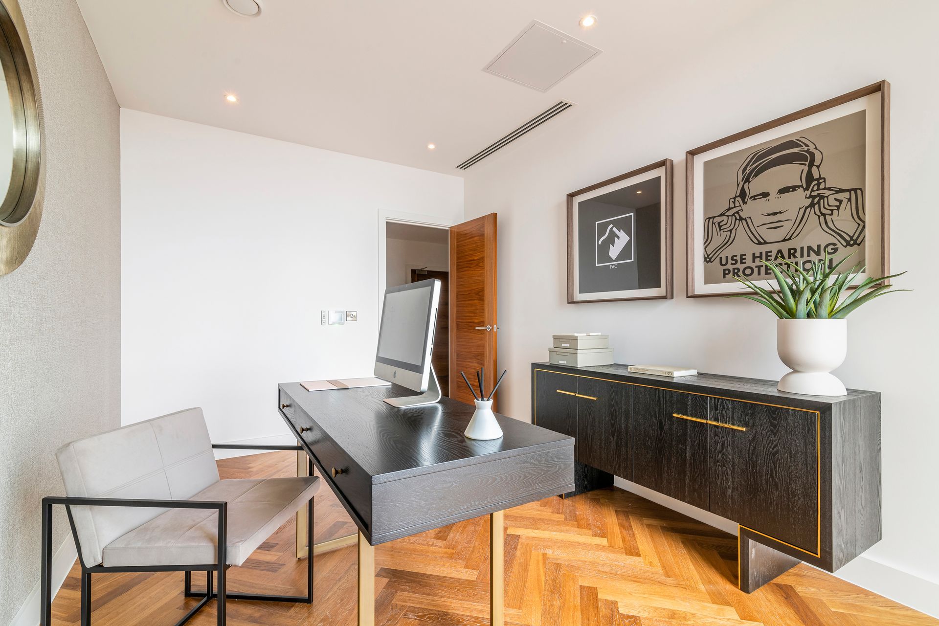 Home office with black desk, chair, and cabinet on wood floor. Artwork and plant.