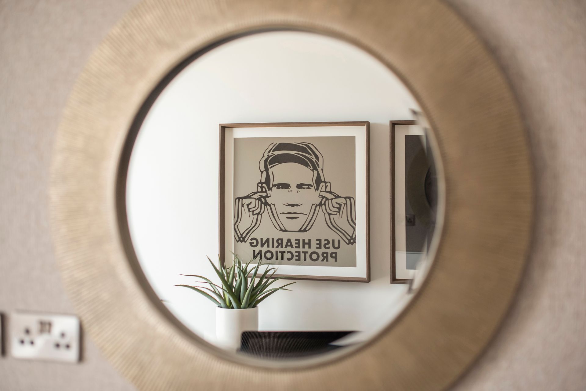 Round mirror reflects a framed poster with a person covering their ears, text reads