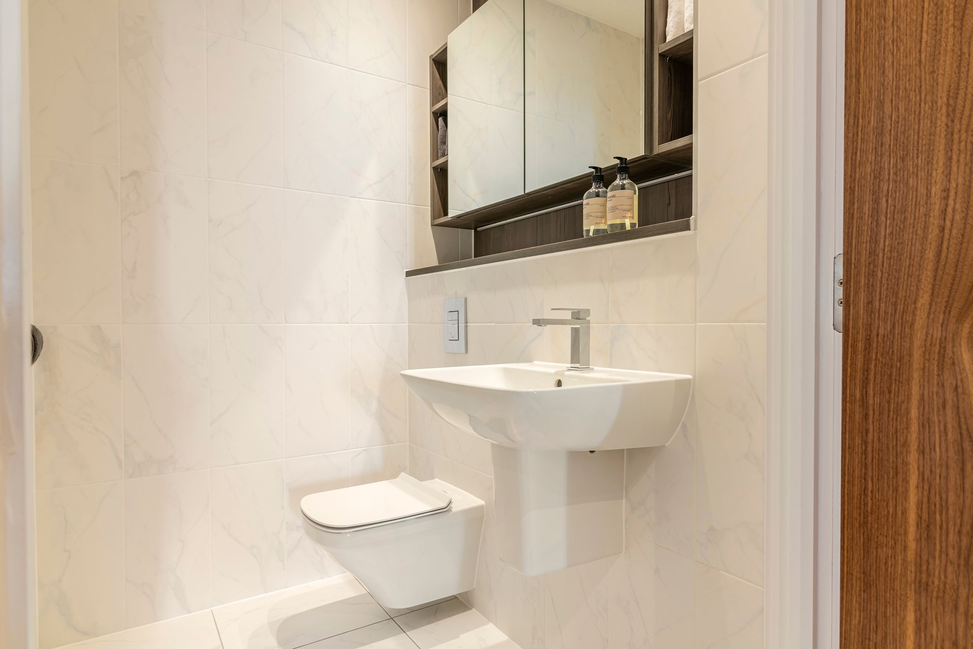 Modern, white bathroom with floating toilet, pedestal sink, and mirrored cabinet.