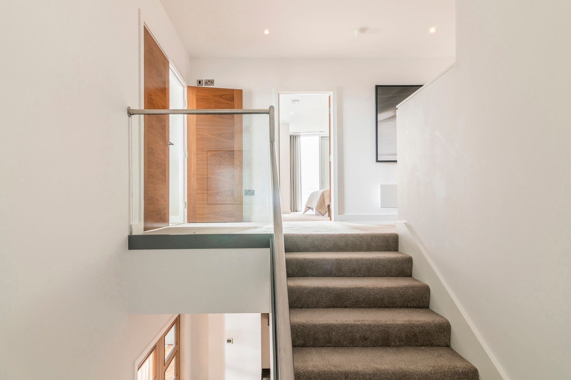 A bright, modern interior with a staircase and hallway, featuring neutral colors, wood doors, and glass railings.