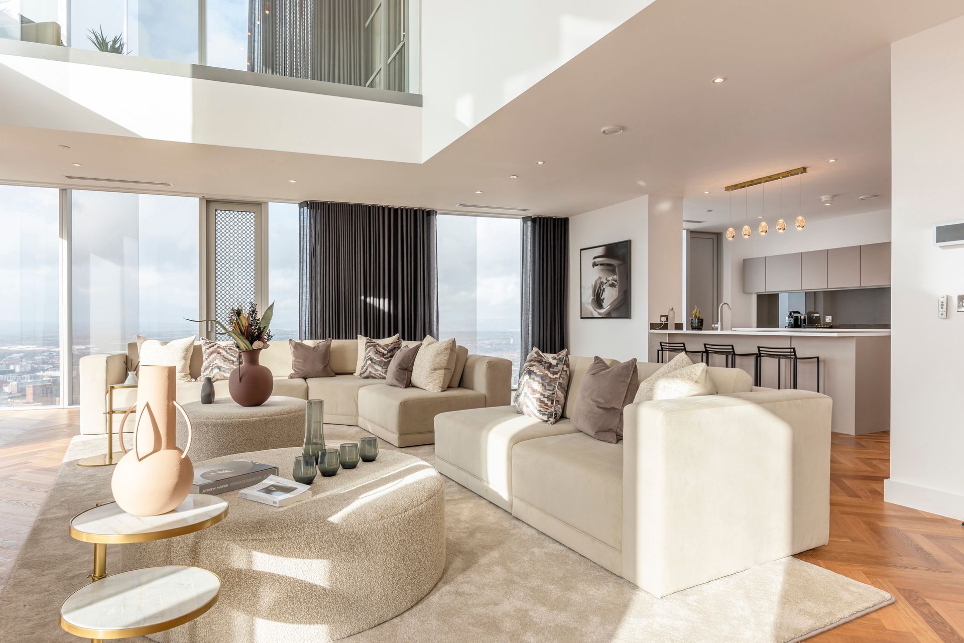 Spacious modern living room with light-colored sofa, round rug, and large windows overlooking a cityscape.