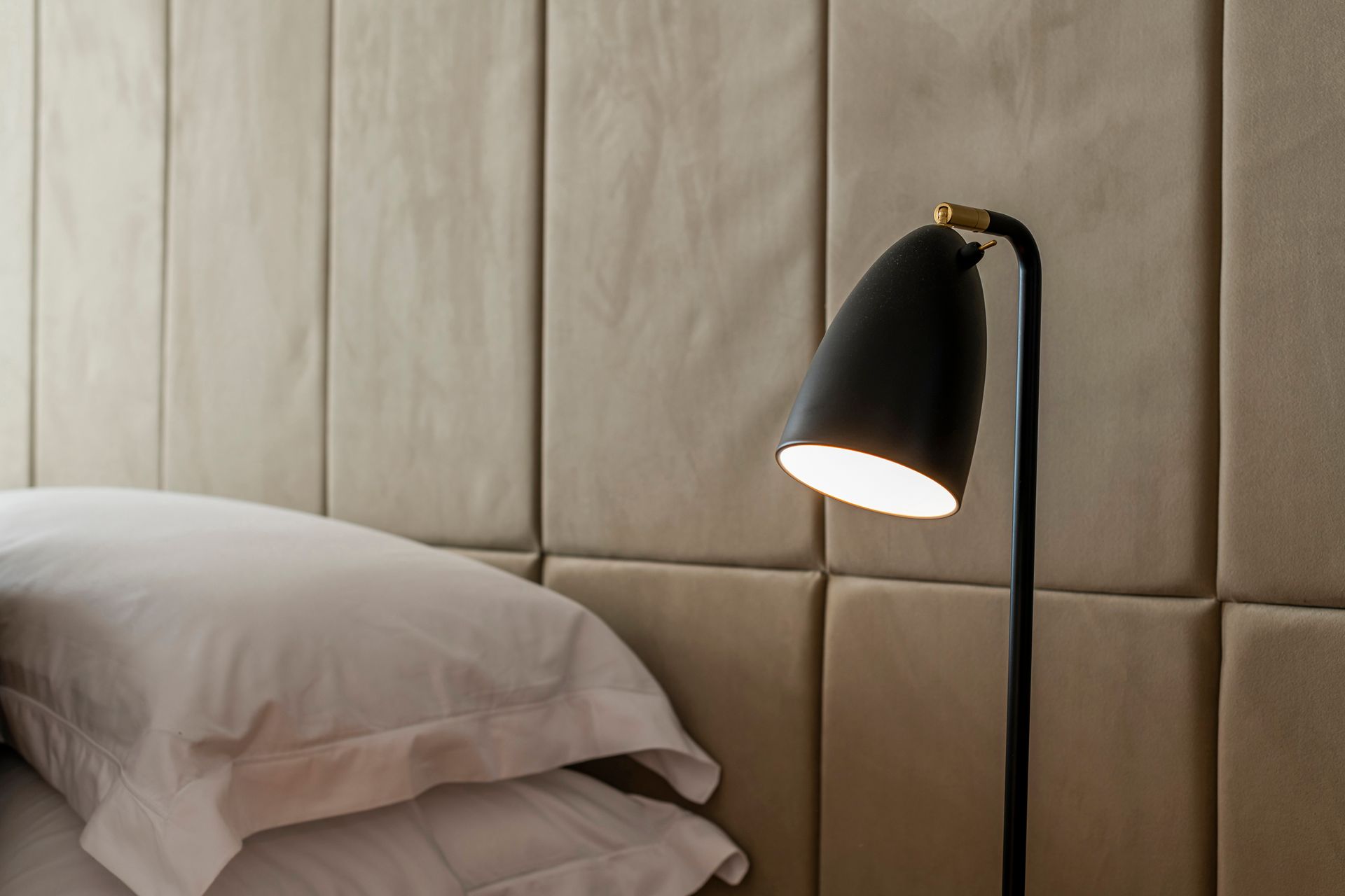 Bed with white pillows, a black bedside lamp, and tan padded wall panels.