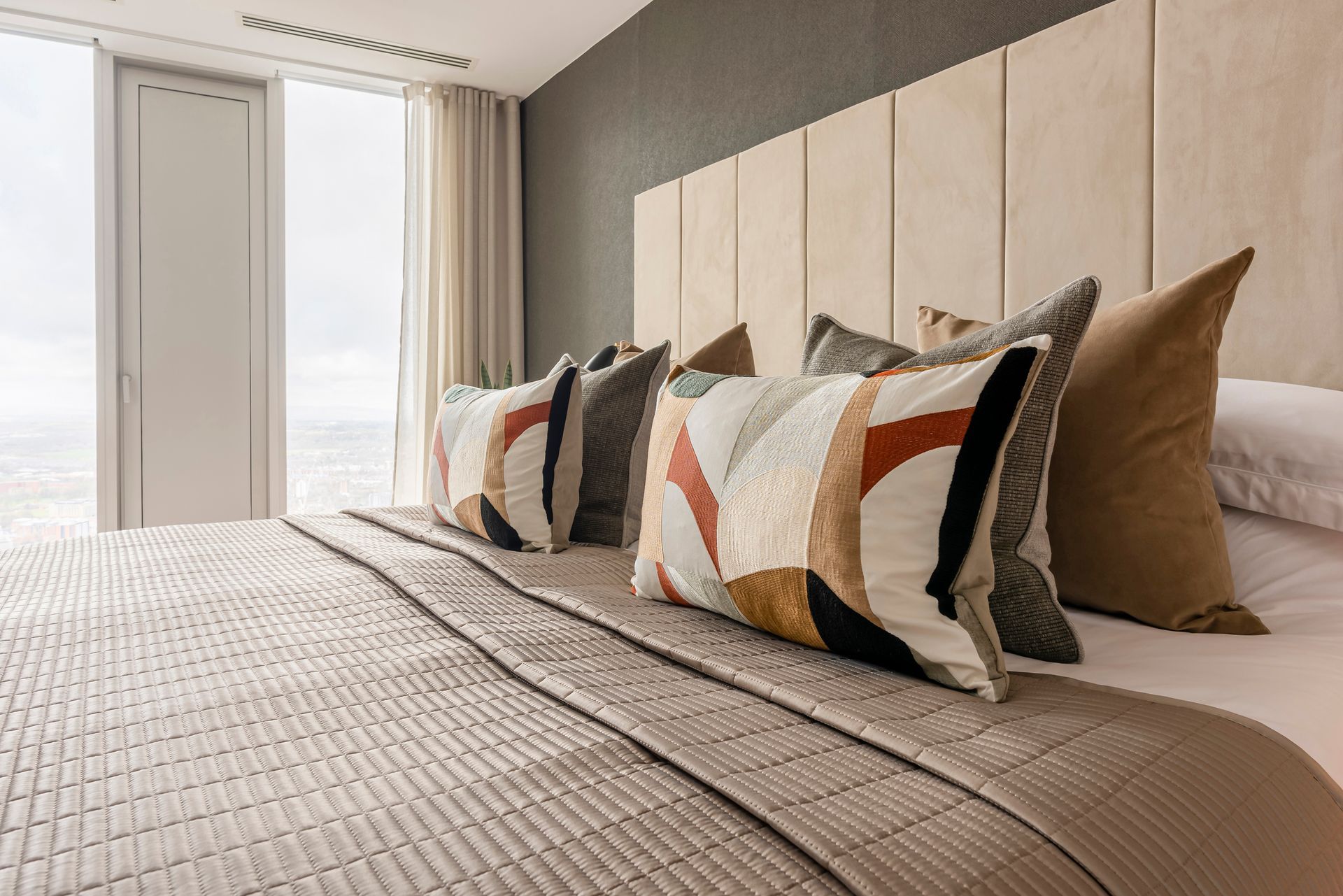 Bed with decorative pillows and a neutral-toned headboard in a modern bedroom.