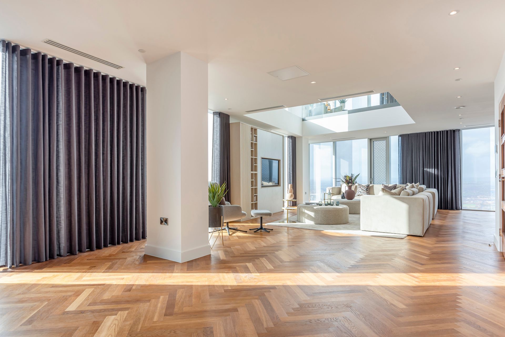 Spacious, modern living room with hardwood floors, floor-to-ceiling windows, and dark grey curtains.