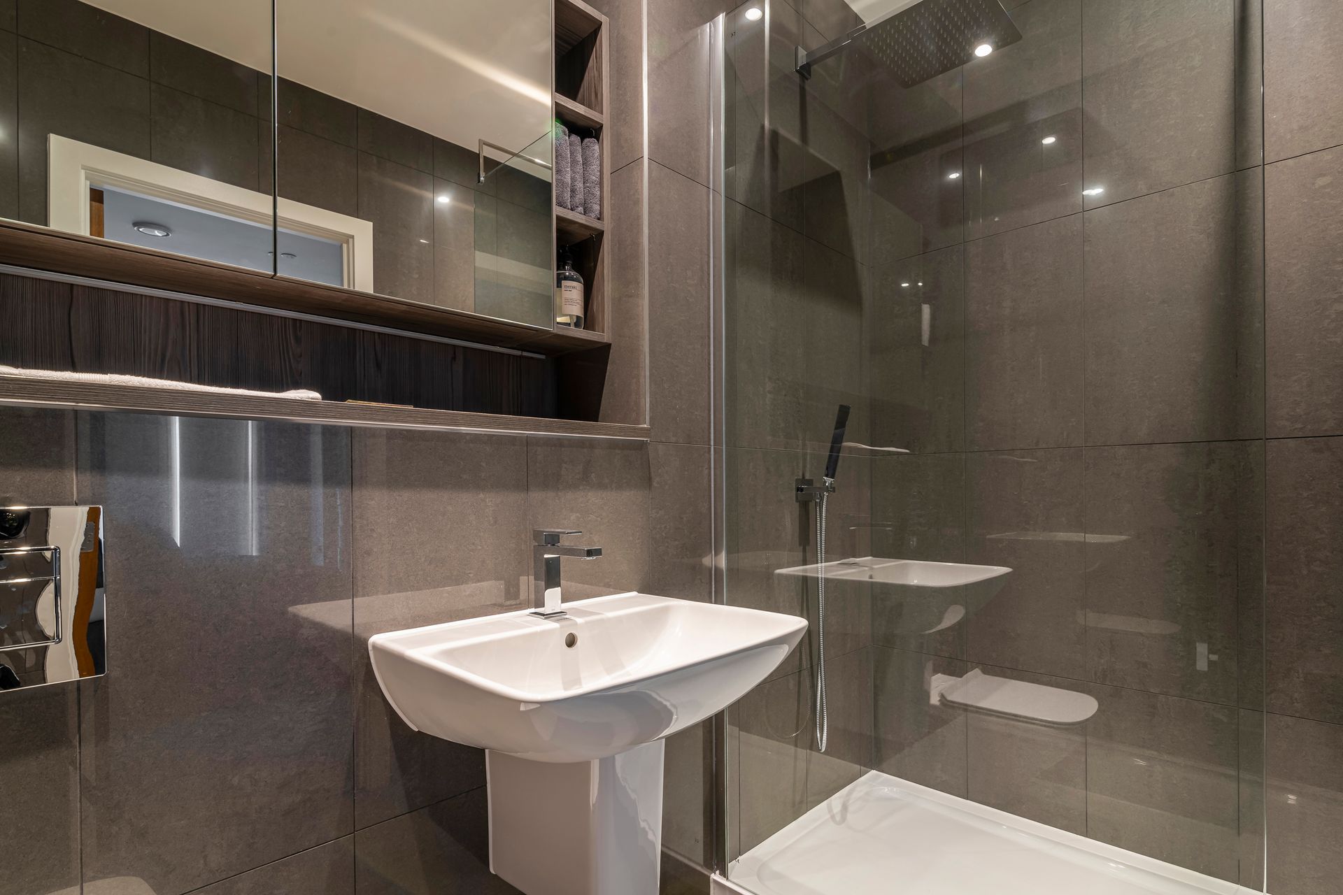Modern gray bathroom with a pedestal sink, walk-in shower, and mirrored medicine cabinet.