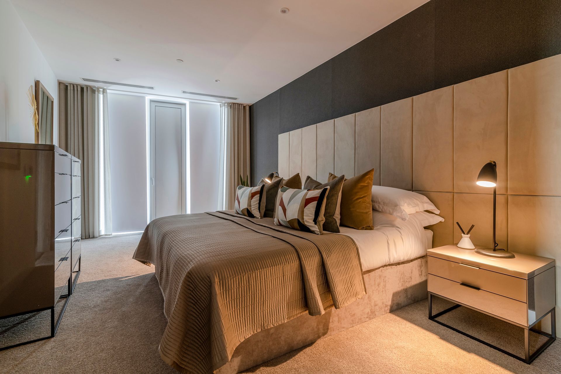 Bedroom with a large bed, nightstand, dresser, neutral colors, and window with blinds.