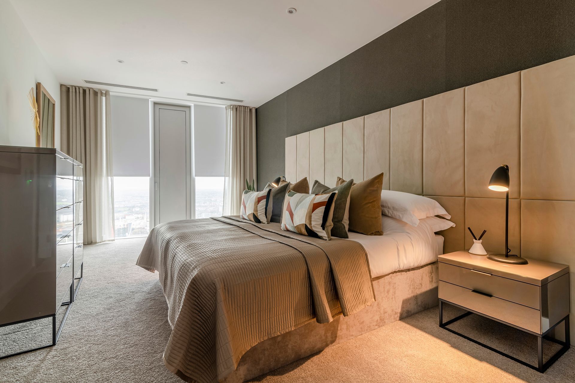 Upscale bedroom with bed, bedside table, dresser, and patterned carpet. Neutral tones and modern design.
