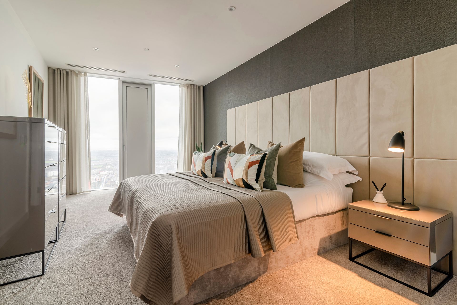 Bedroom with a bed, nightstand, and dresser. Neutral tones with a large window and carpet.
