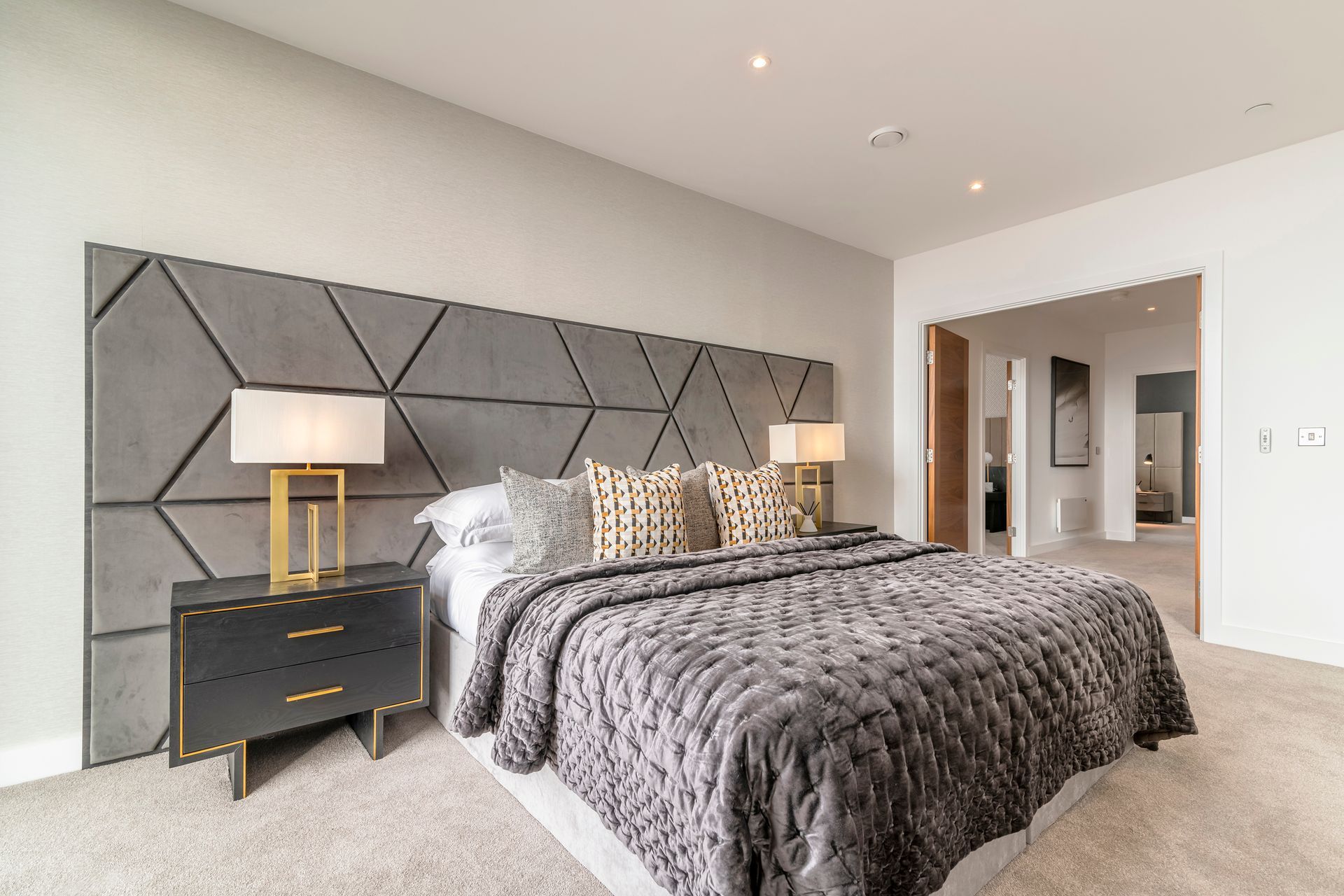 Modern bedroom with gray geometric headboard, bed, bedside tables, and doorway to another room.