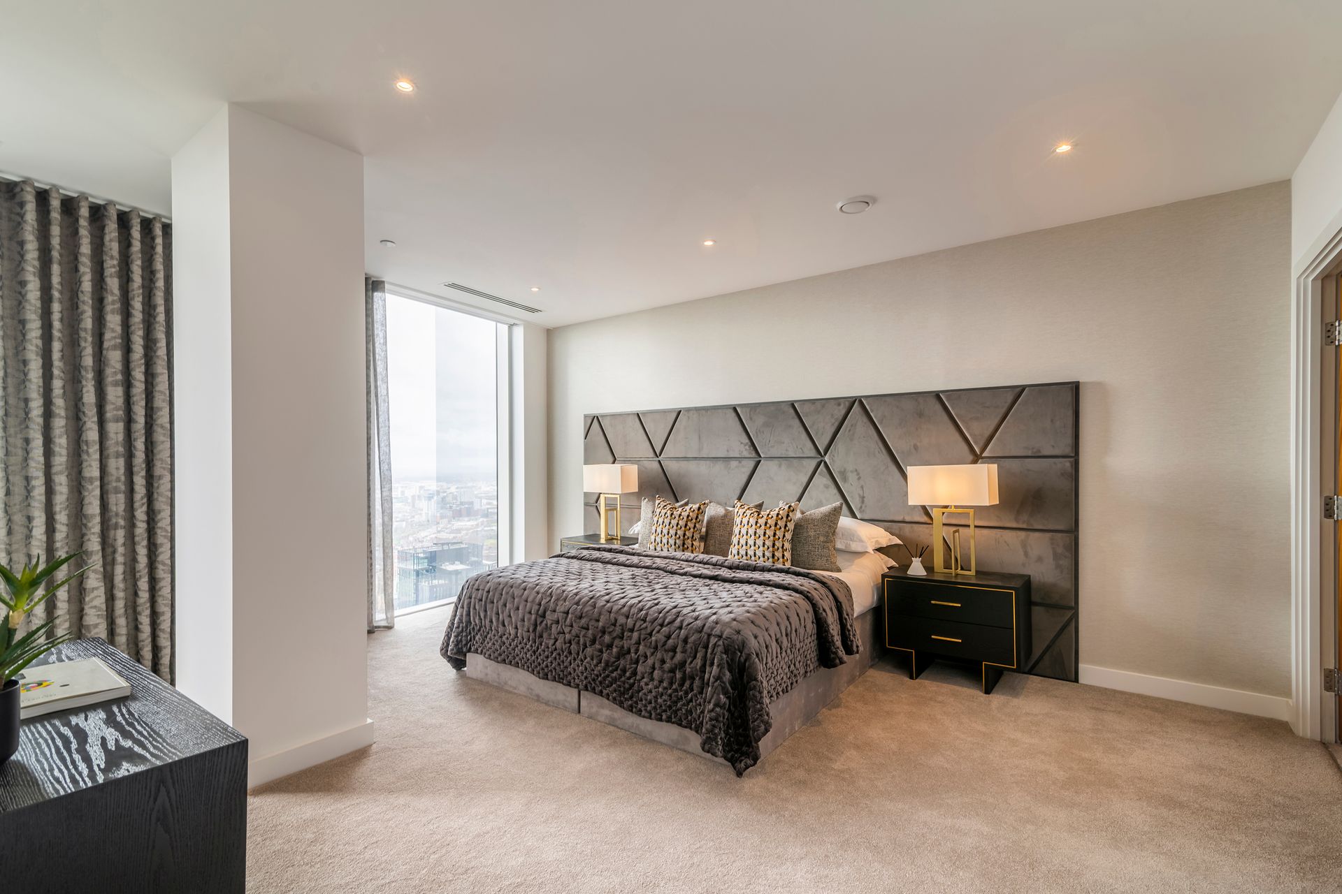 Modern bedroom with gray patterned headboard, bed, and carpet; window with cityscape view.