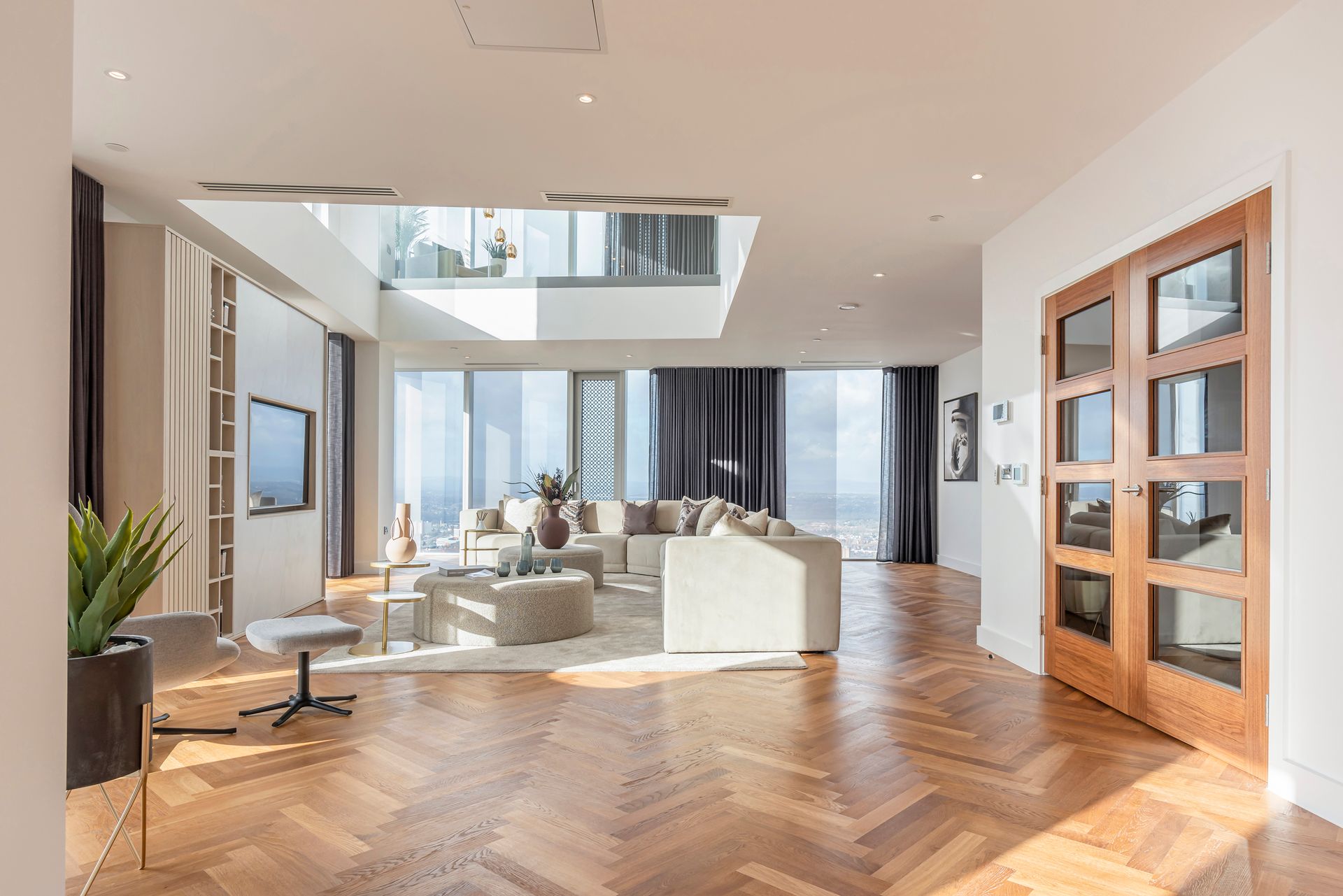 Spacious living room with wood floors, large windows, beige sectional sofa, and a double glass door.
