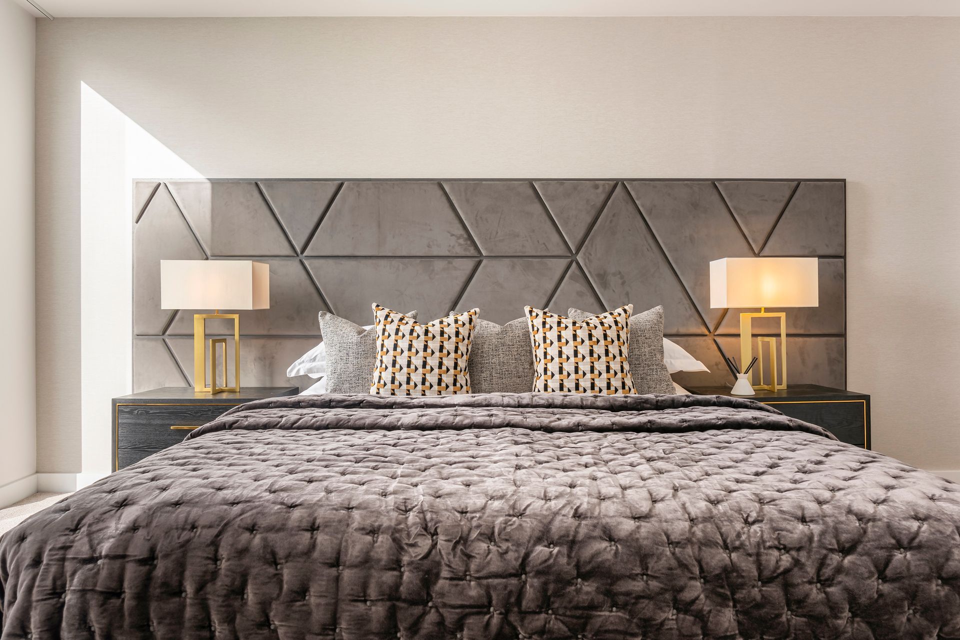 Bedroom with a large bed, gray textured headboard, bedside lamps, and decorative pillows.
