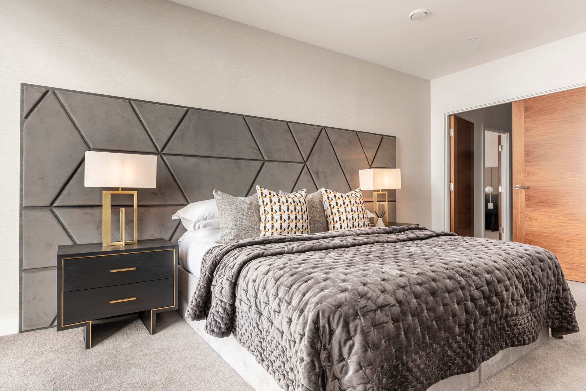Gray-toned bedroom with geometric headboard, two nightstands, lamps, and a bed with a quilted cover.