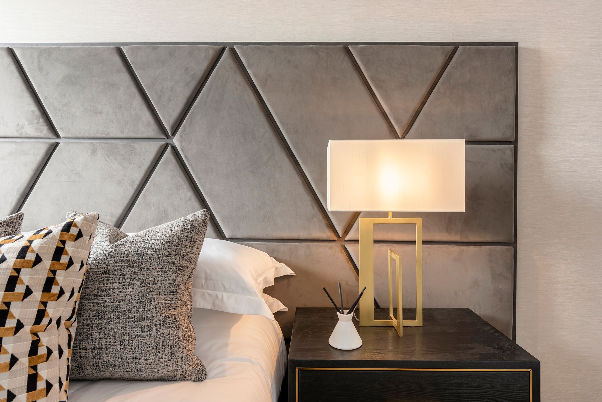 Bedroom with gray geometric headboard, bedside table with lamp, and pillows.