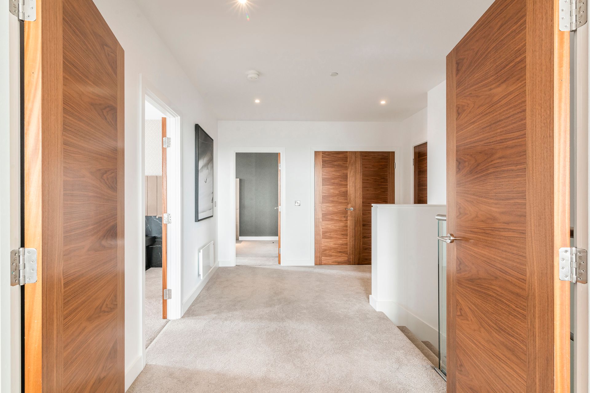 Hallway with wood doors, white walls, and beige carpet.