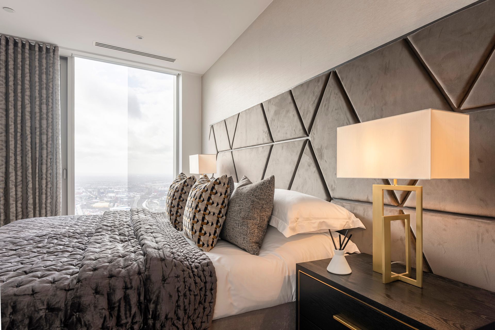 Bedroom with a large bed, decorative headboard, nightstand, and window with a city view.