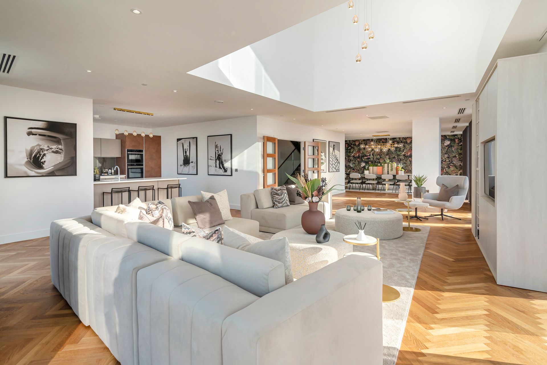 Modern open-plan living room with light-colored sofa, hardwood floors, large skylight, and artwork.