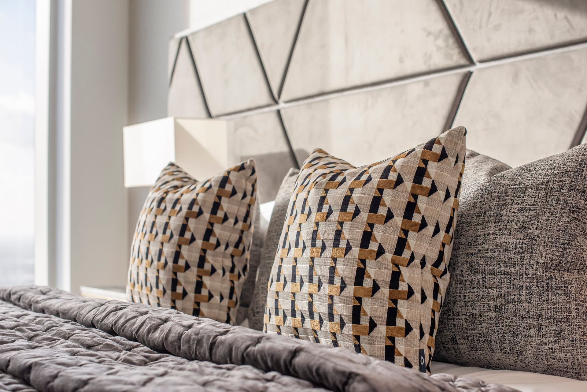 Bed with patterned pillows and geometric headboard.
