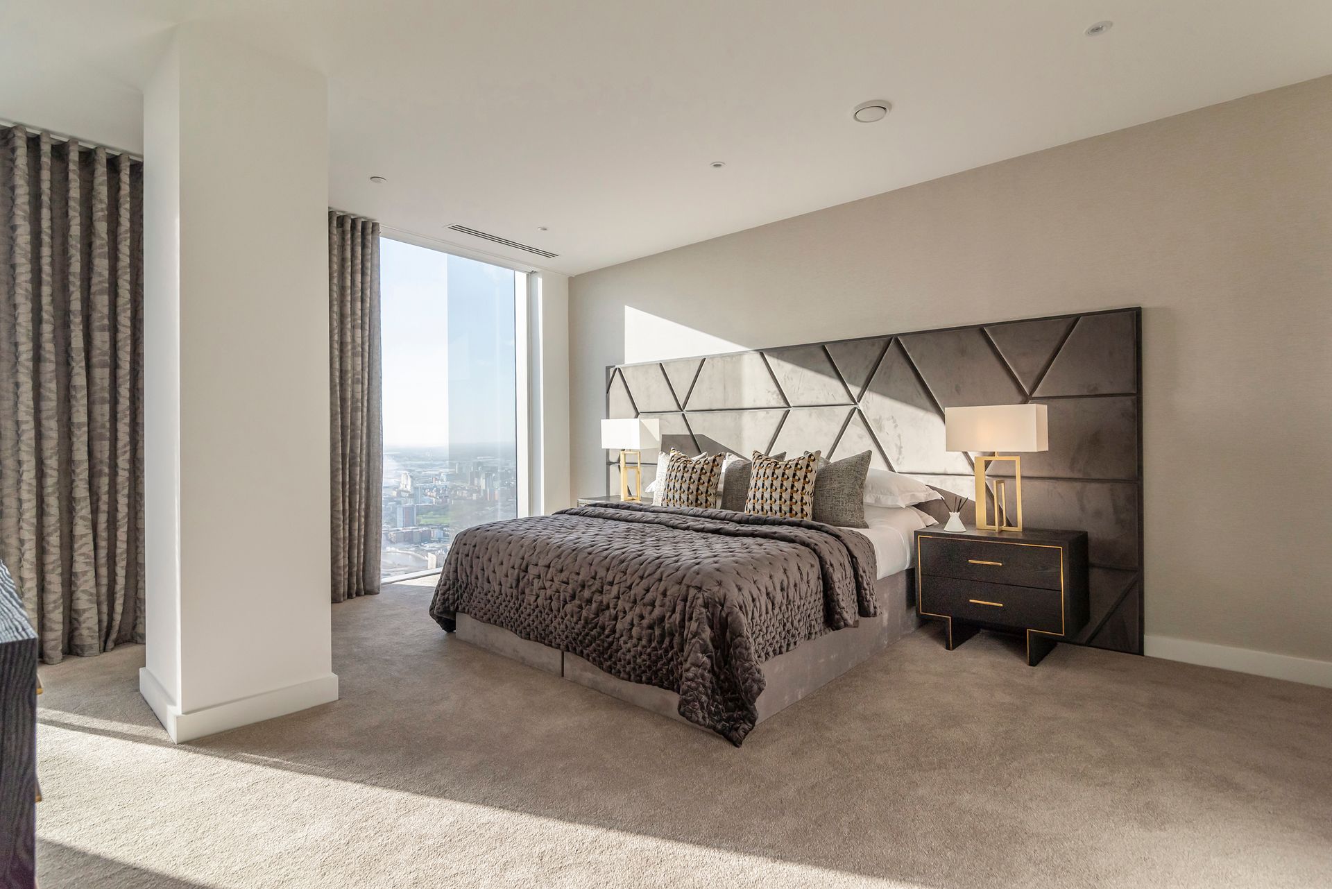 Bedroom with a large bed, geometric headboard, and city view through a large window.