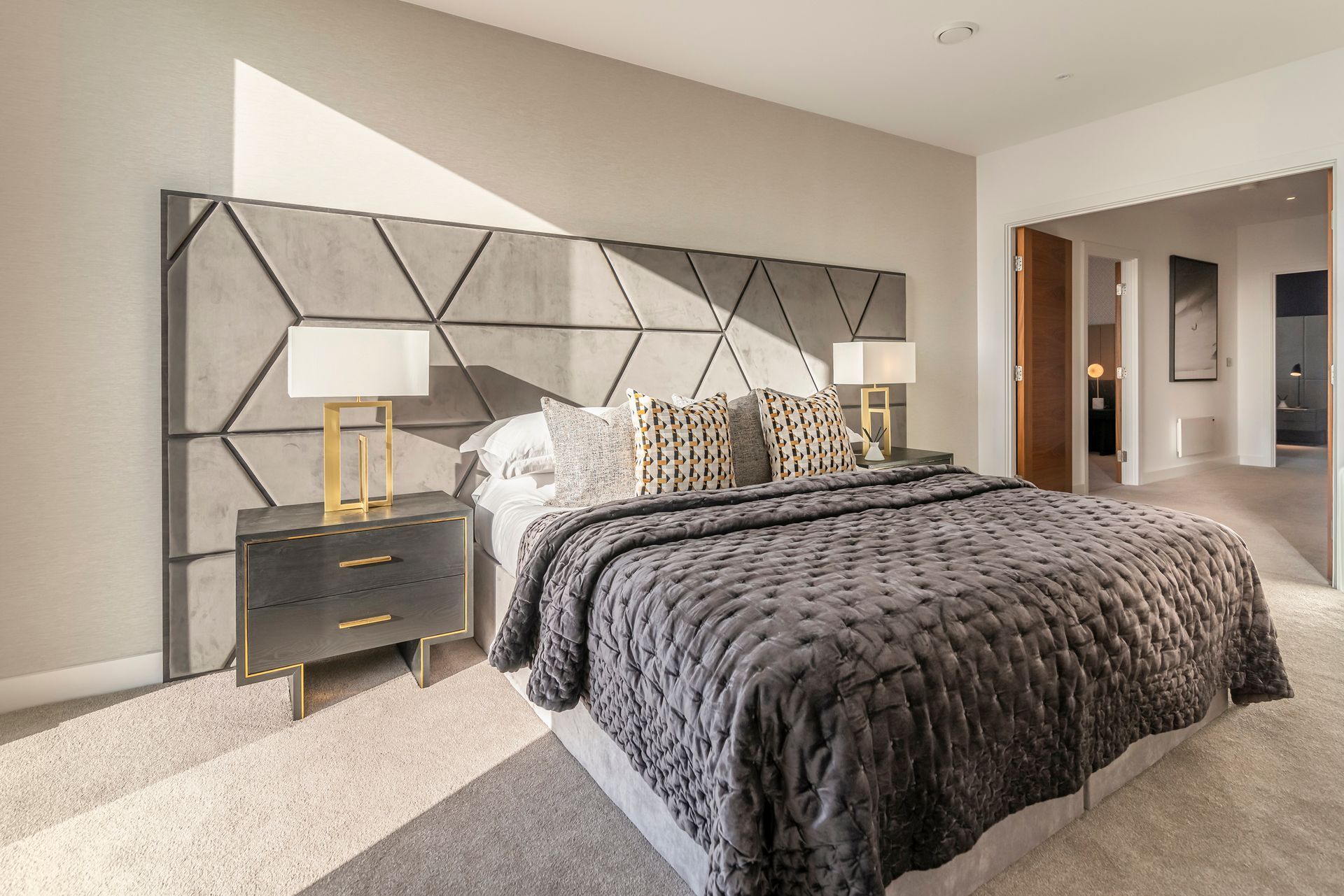 Bedroom with a geometric headboard, two nightstands, a gray bedspread, and a carpeted floor.