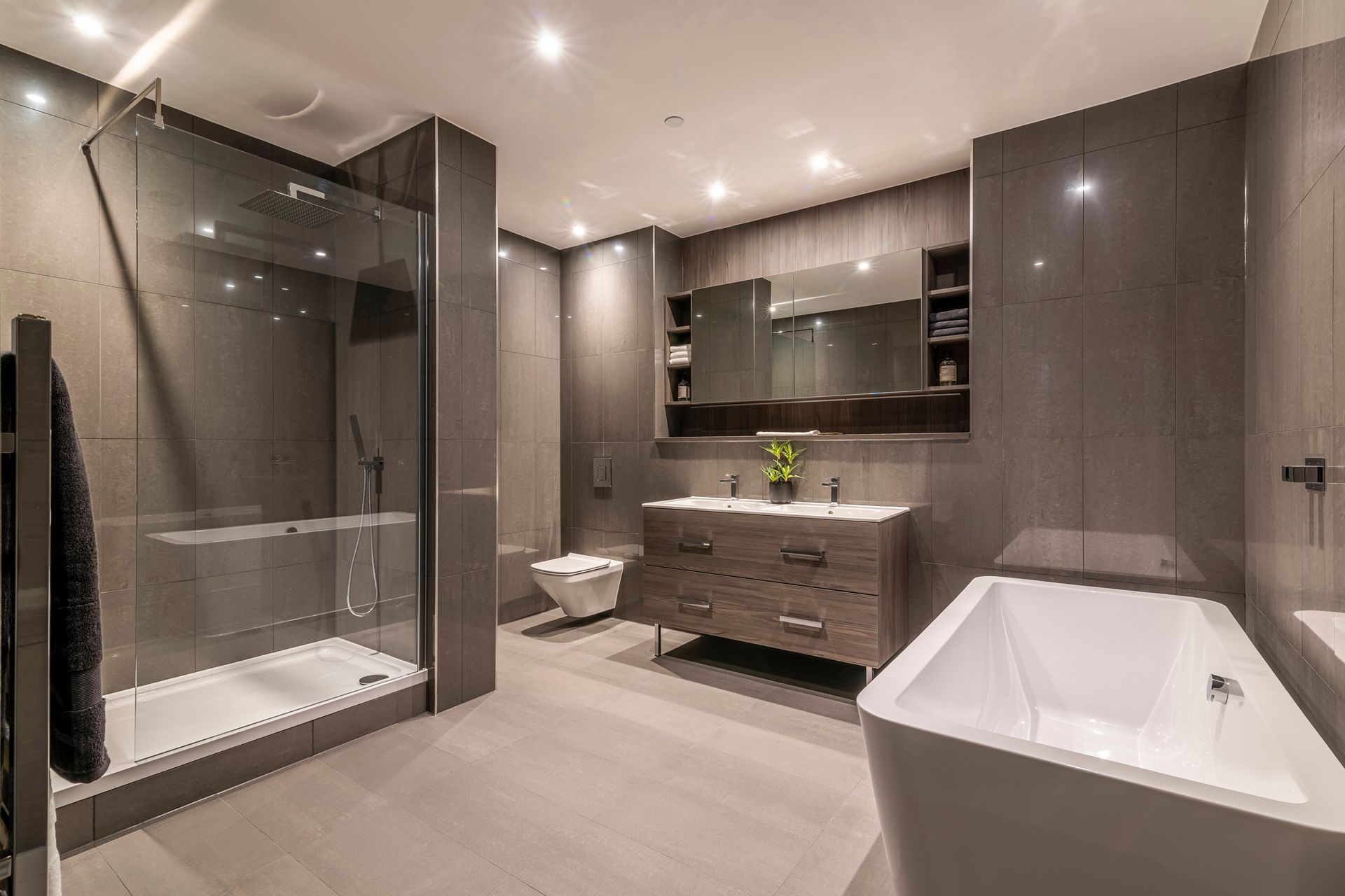 Modern gray bathroom with shower, toilet, double sink, and freestanding tub.