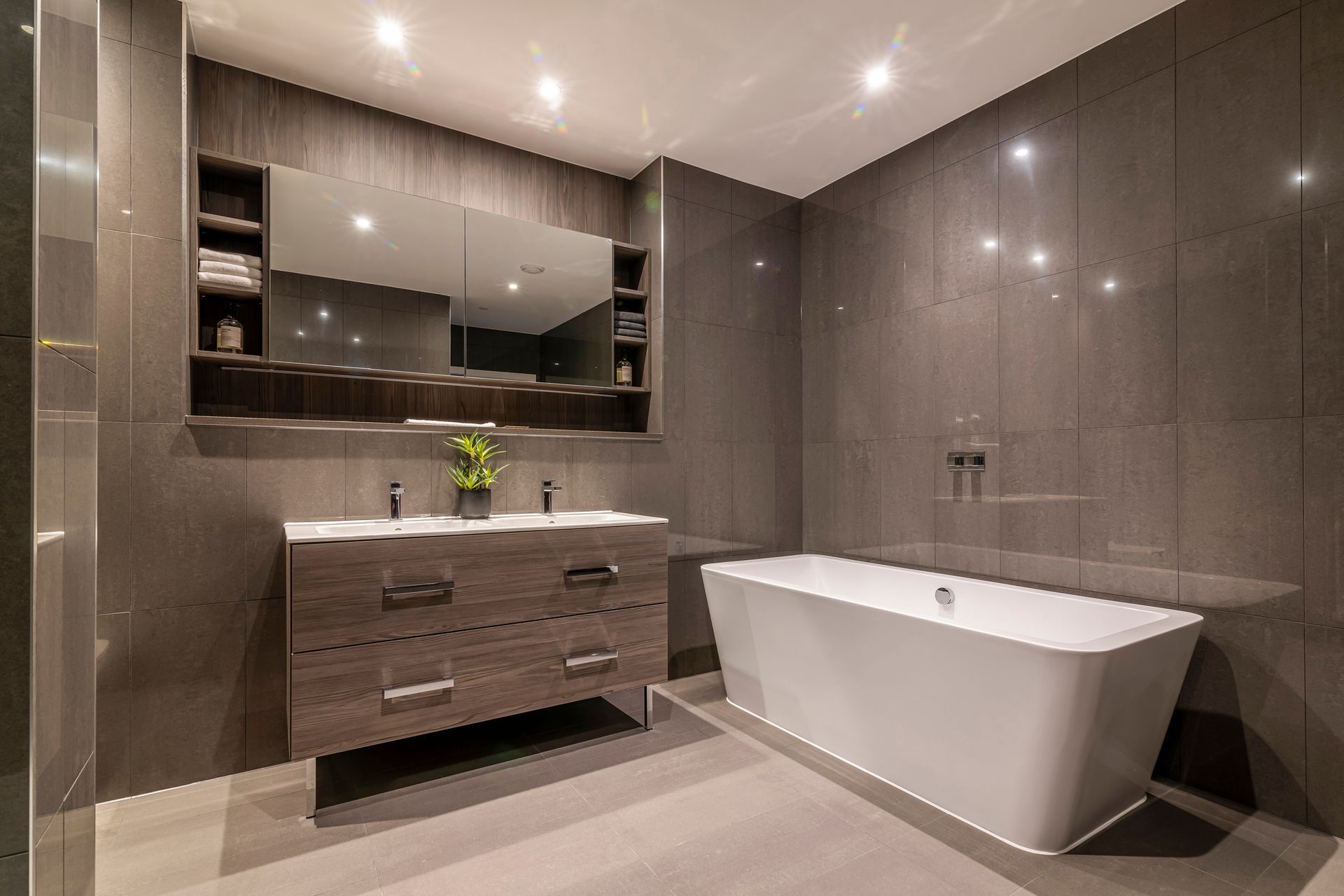 Modern bathroom with a bathtub, vanity, and gray tile walls.