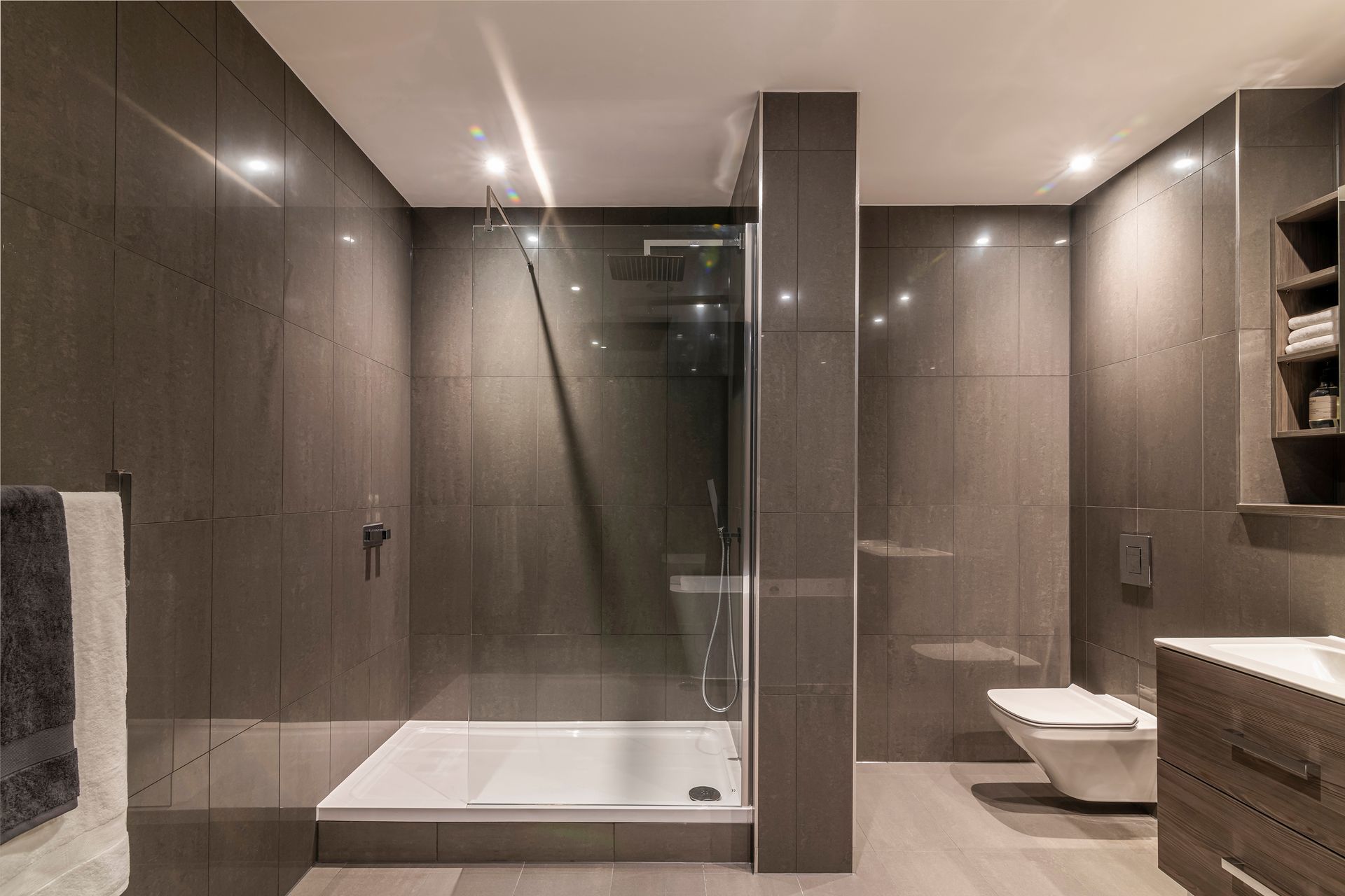 Modern bathroom with gray tiles, glass shower, and toilet.