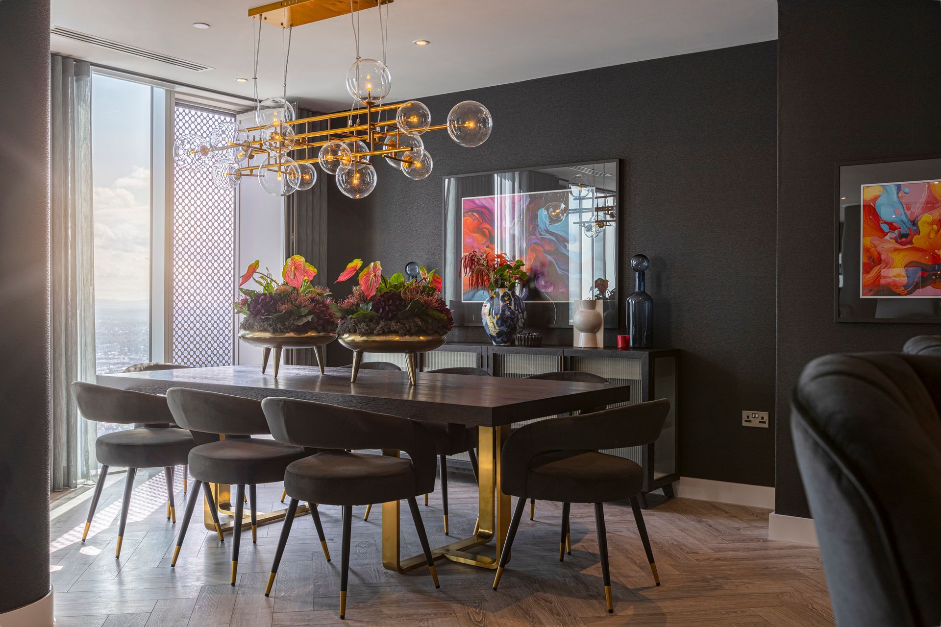Dining room with dark walls, large table, stylish chairs, and modern gold chandelier.