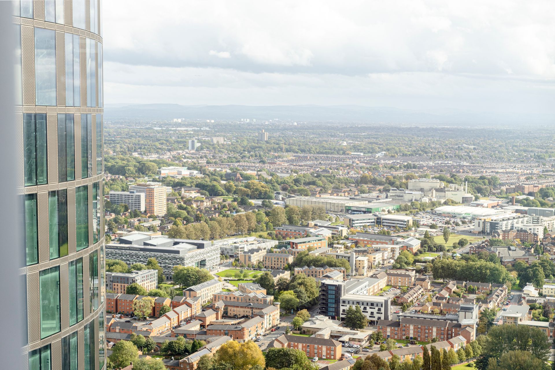 Cityscape view from a high-rise building with a curved glass exterior, buildings and trees in the distance.