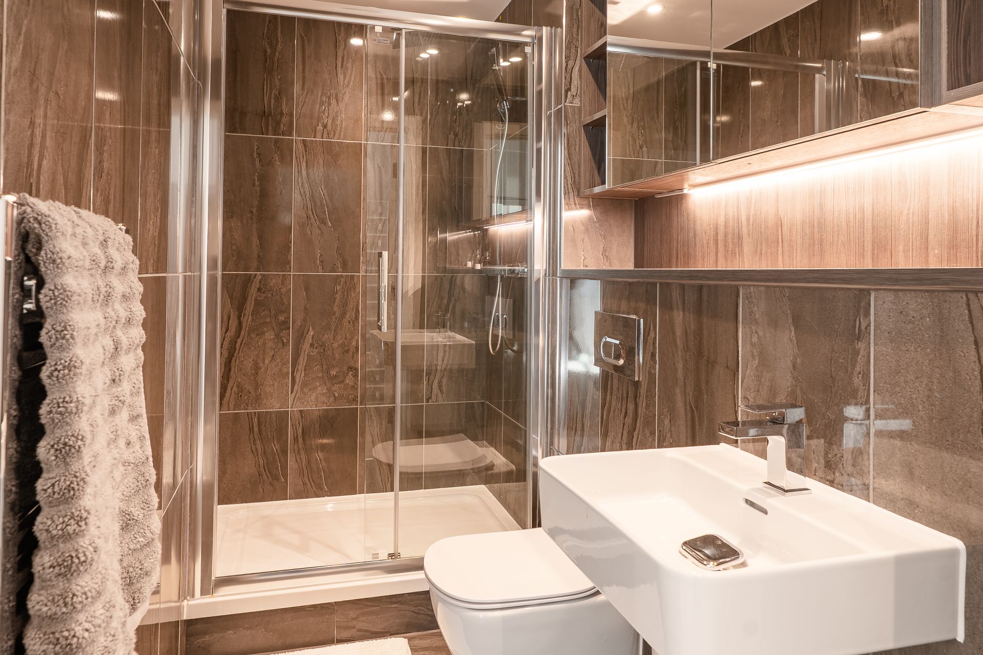 Modern bathroom with brown tile walls, glass shower, white sink, and toilet.