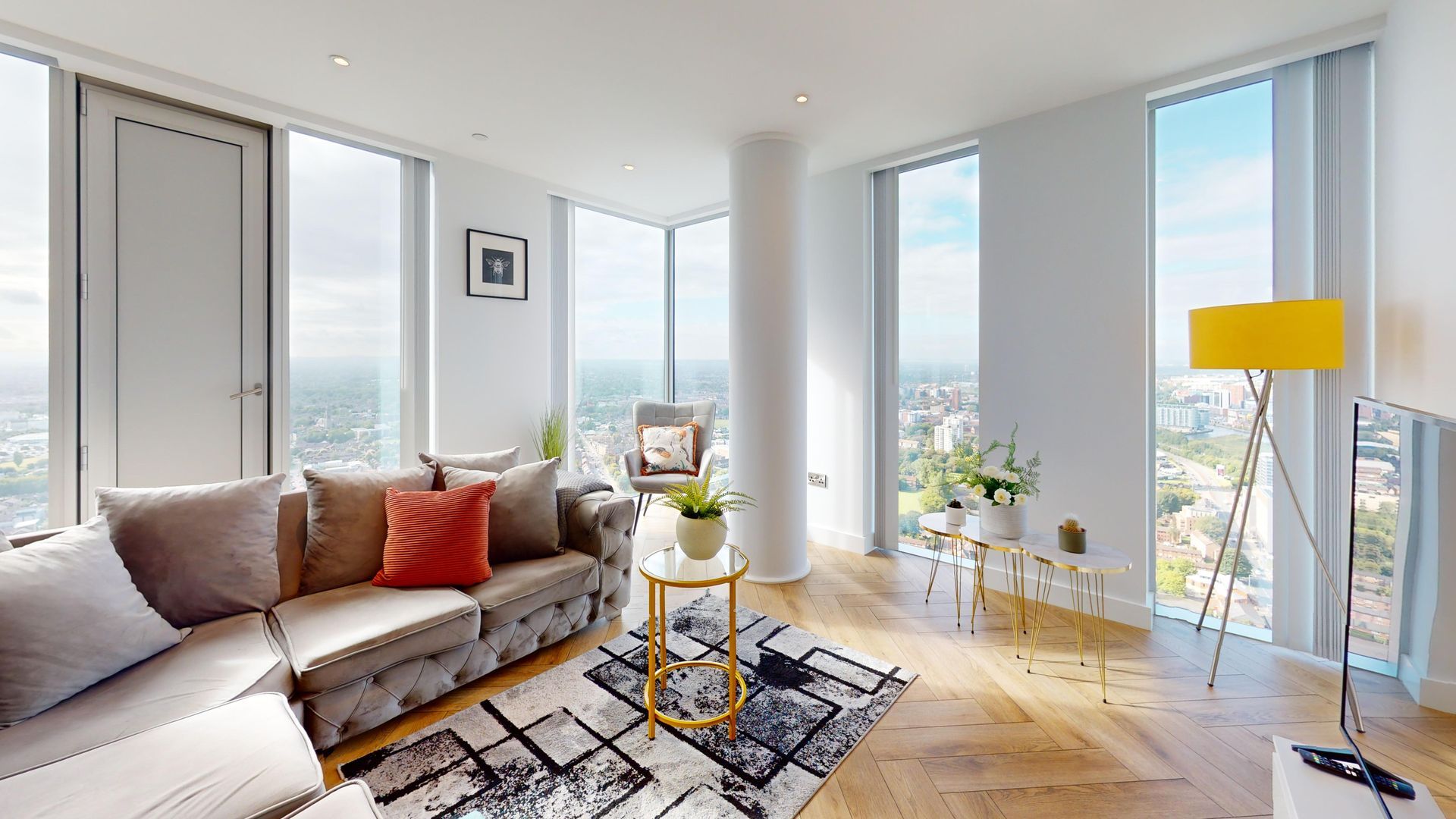 Modern living room with floor-to-ceiling windows, cityscape view, grey sofa, yellow lamp, and marble coffee table.