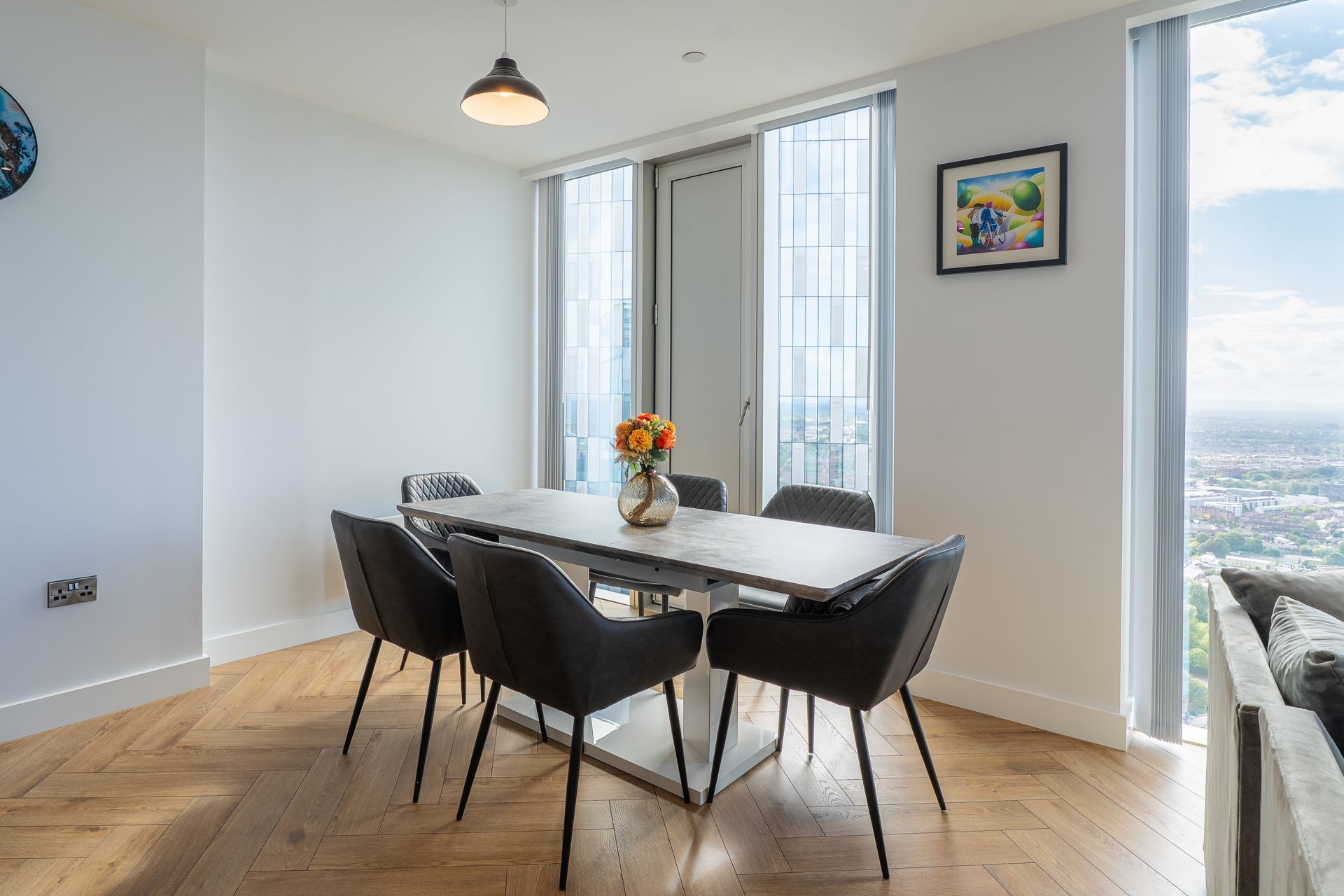 Dining room with table, chairs, flowers, and a large window with city view.