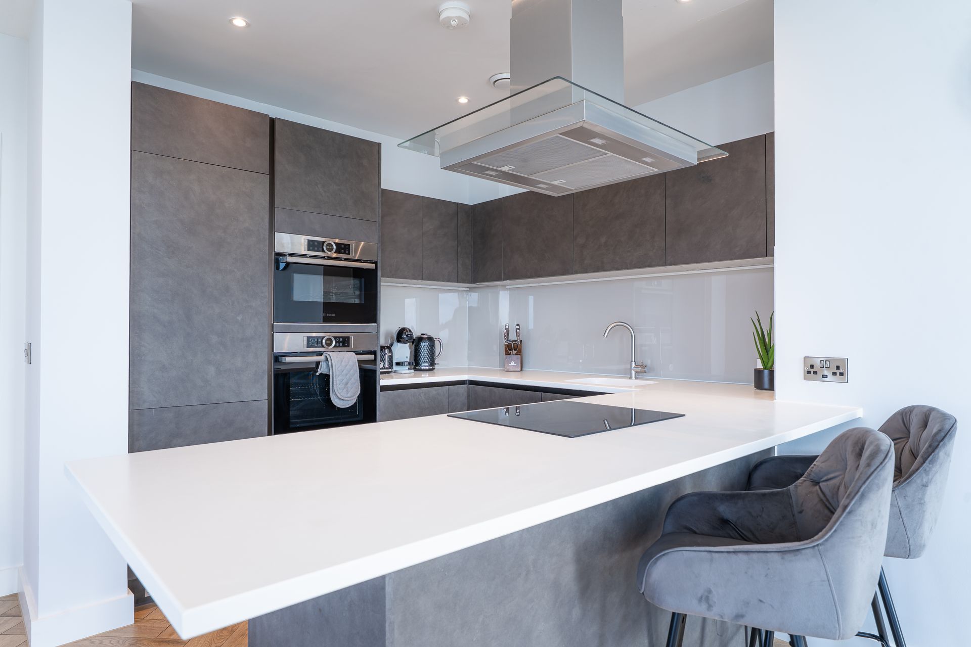 Modern kitchen with gray cabinets, white countertop, stainless steel appliances, and two gray bar stools.