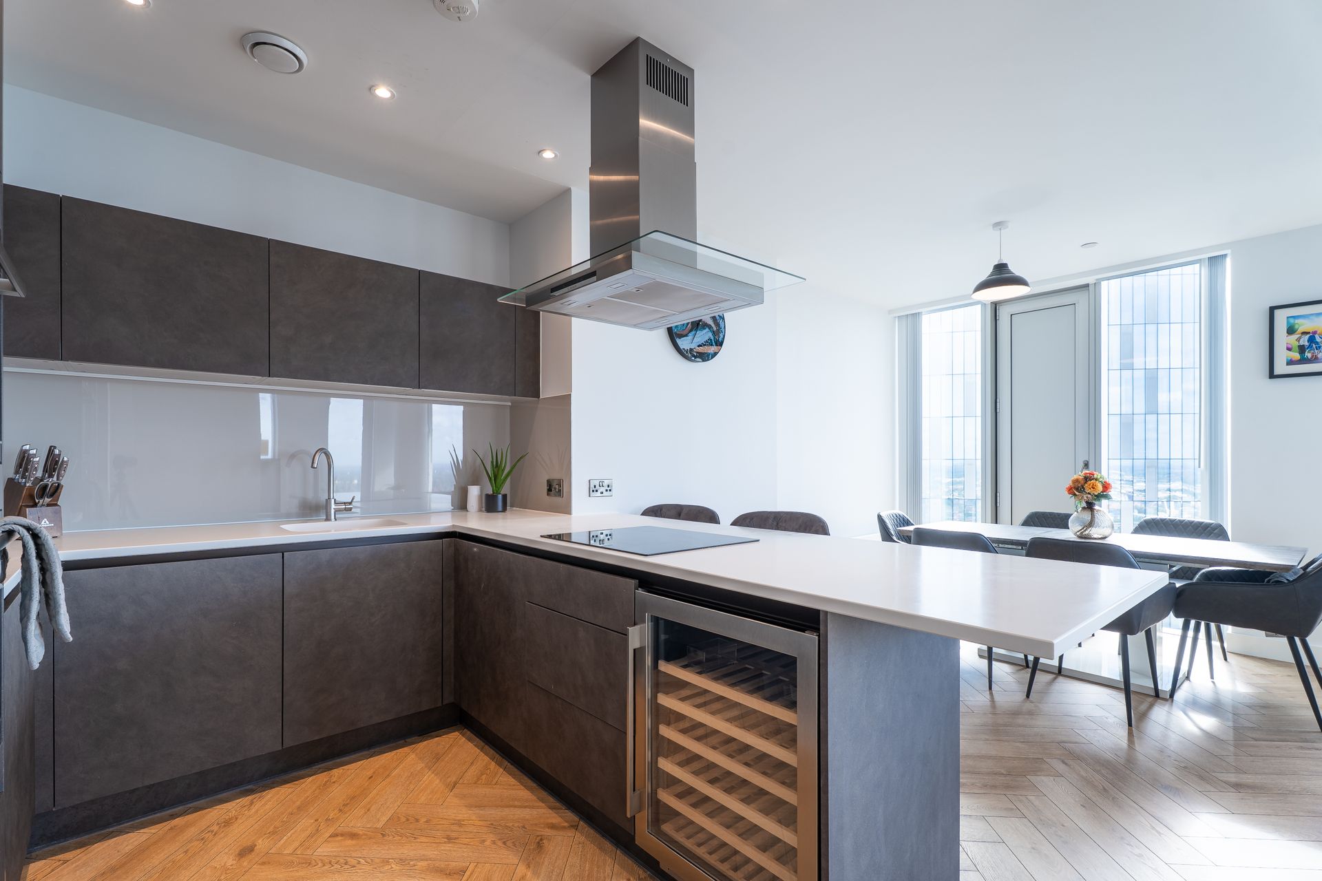 Modern kitchen with gray cabinets, white countertops, island with wine fridge, and dining area.
