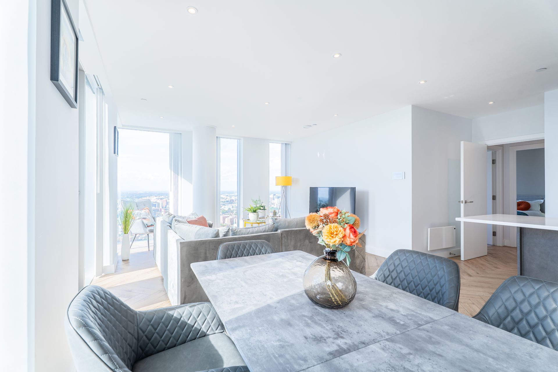 Spacious, bright living room with dining area and city views, featuring a table with a flower vase.