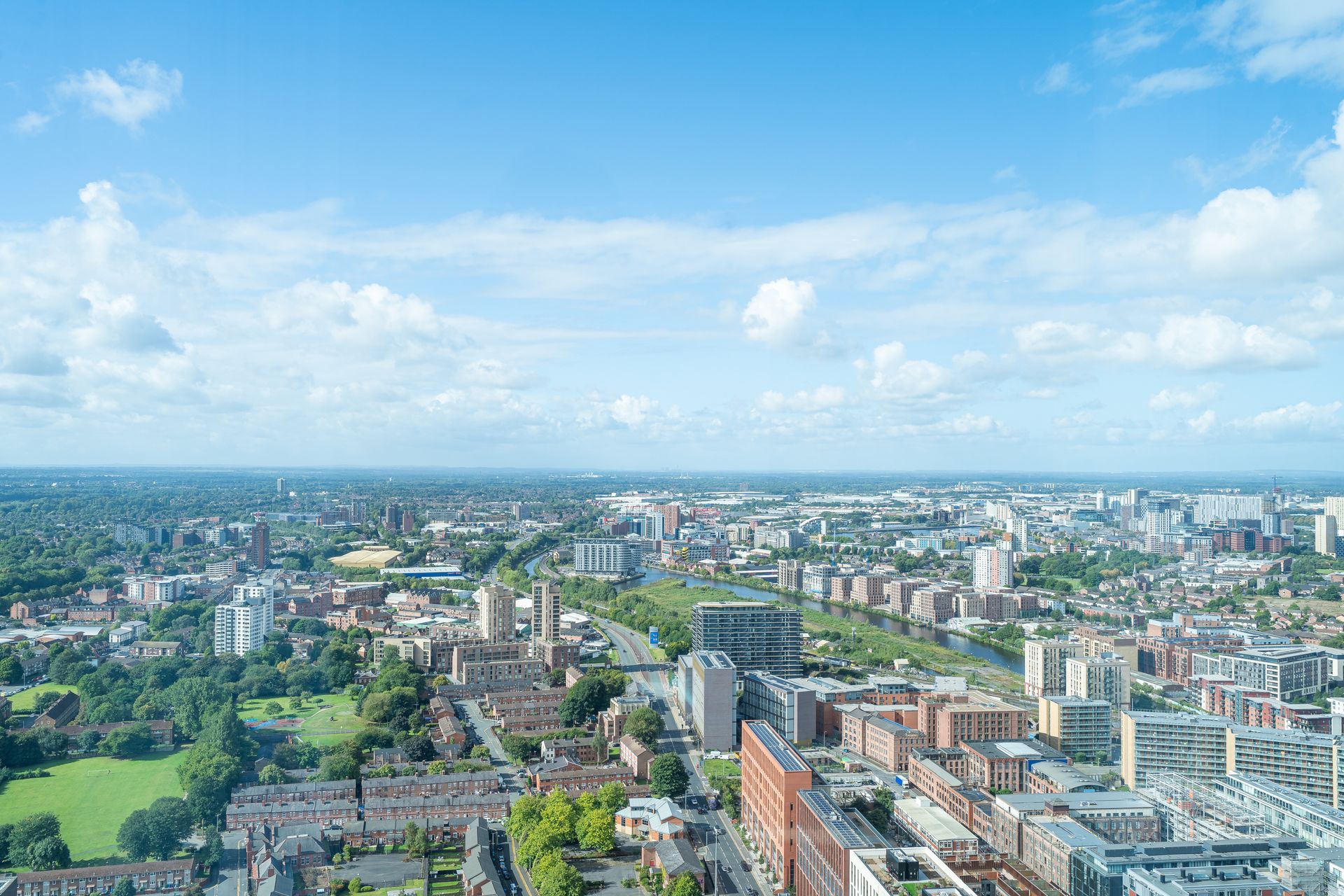 City skyline under a blue sky, with buildings, a park, and a river visible.