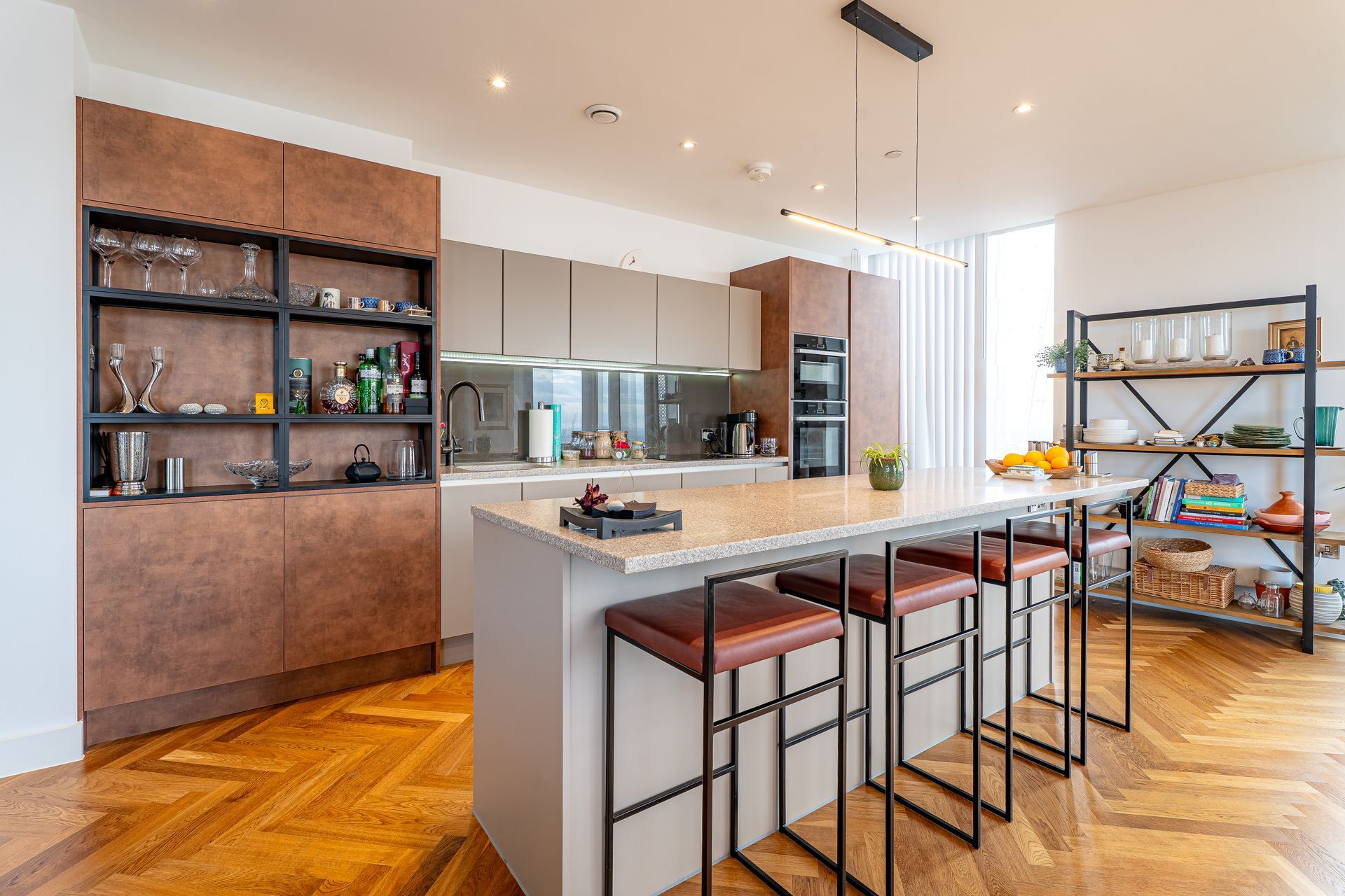 Modern kitchen with island, brown and gray cabinetry, bar stools, and wooden flooring.