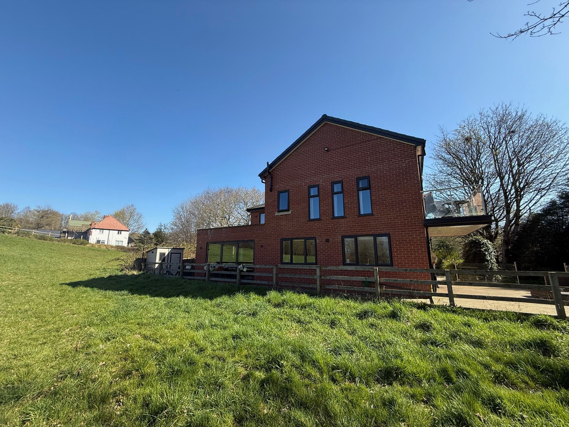 Red brick house with black-framed windows on a grassy hillside under a clear blue sky.