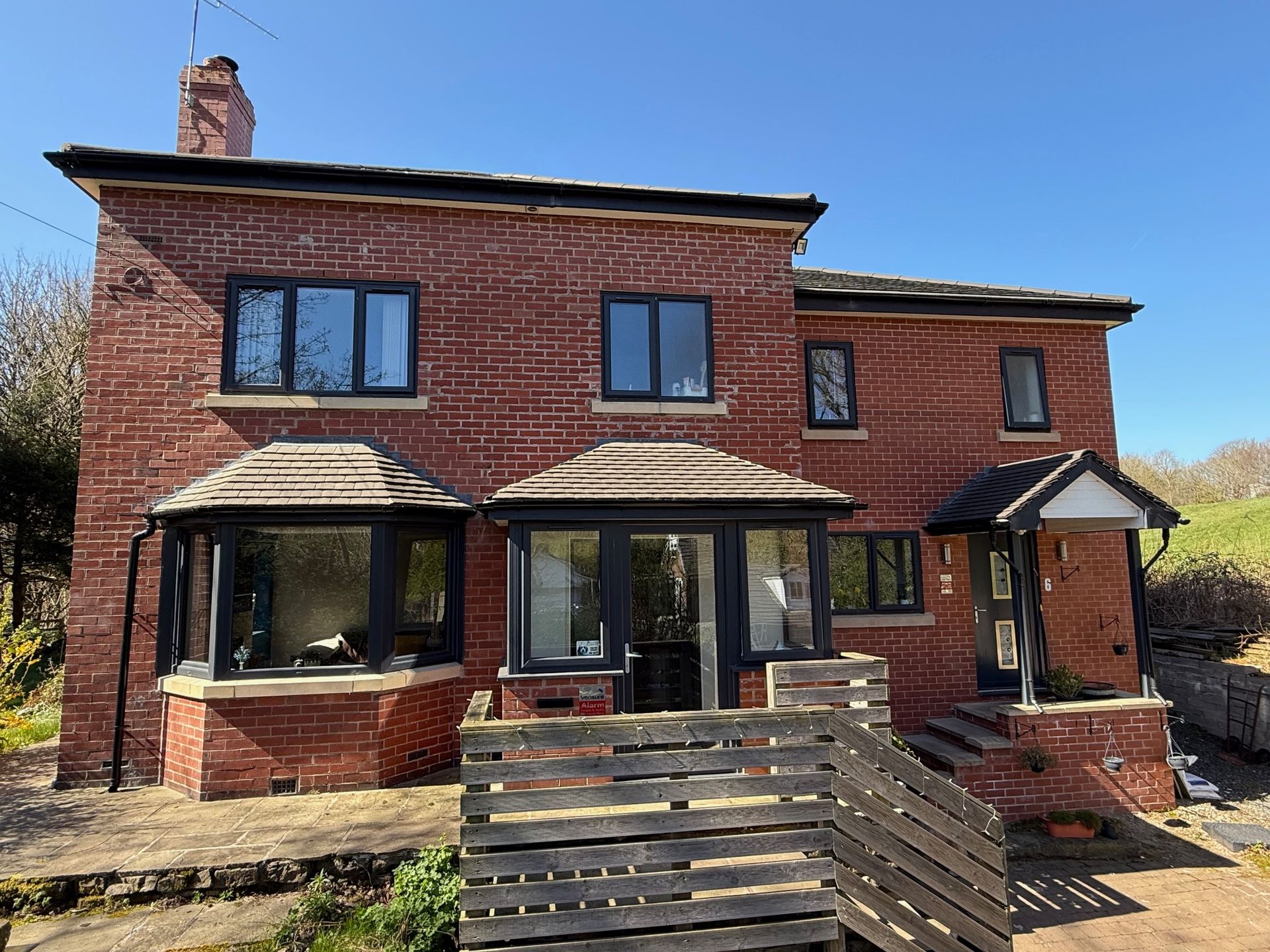 Red brick house with black-framed windows and a wooden deck on a sunny day.