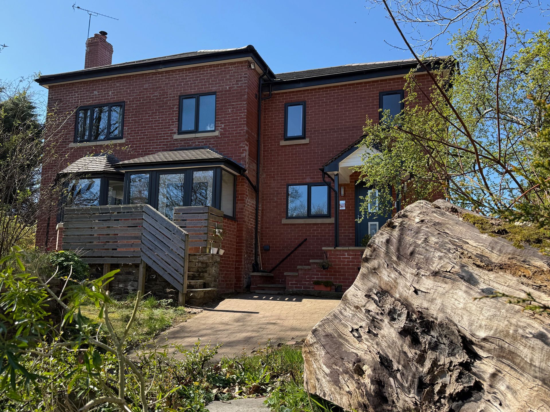 Red brick house with multiple windows and a small porch on a sunny day.