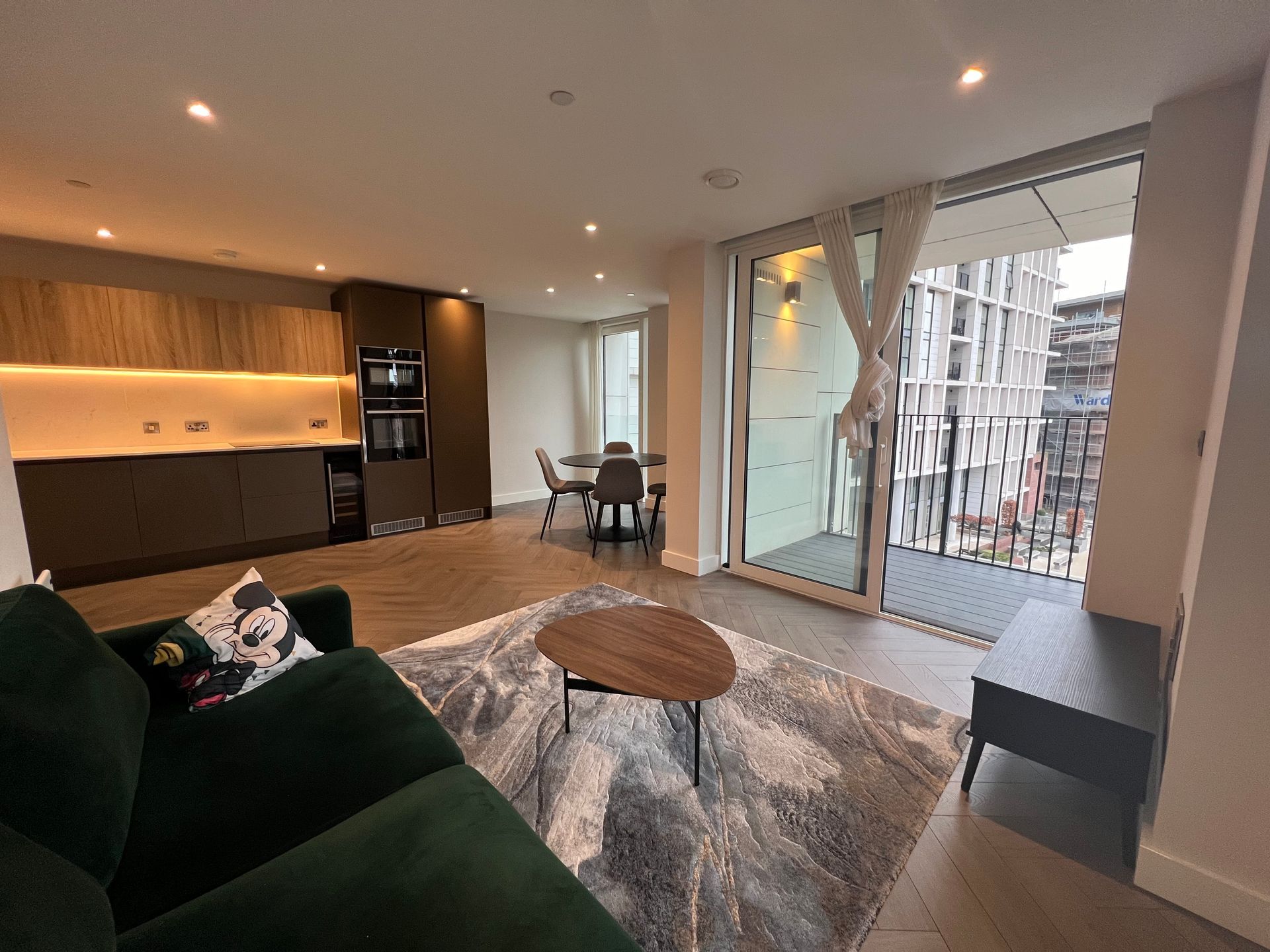 Modern apartment interior with green sofa, kitchen, dining area, and balcony.