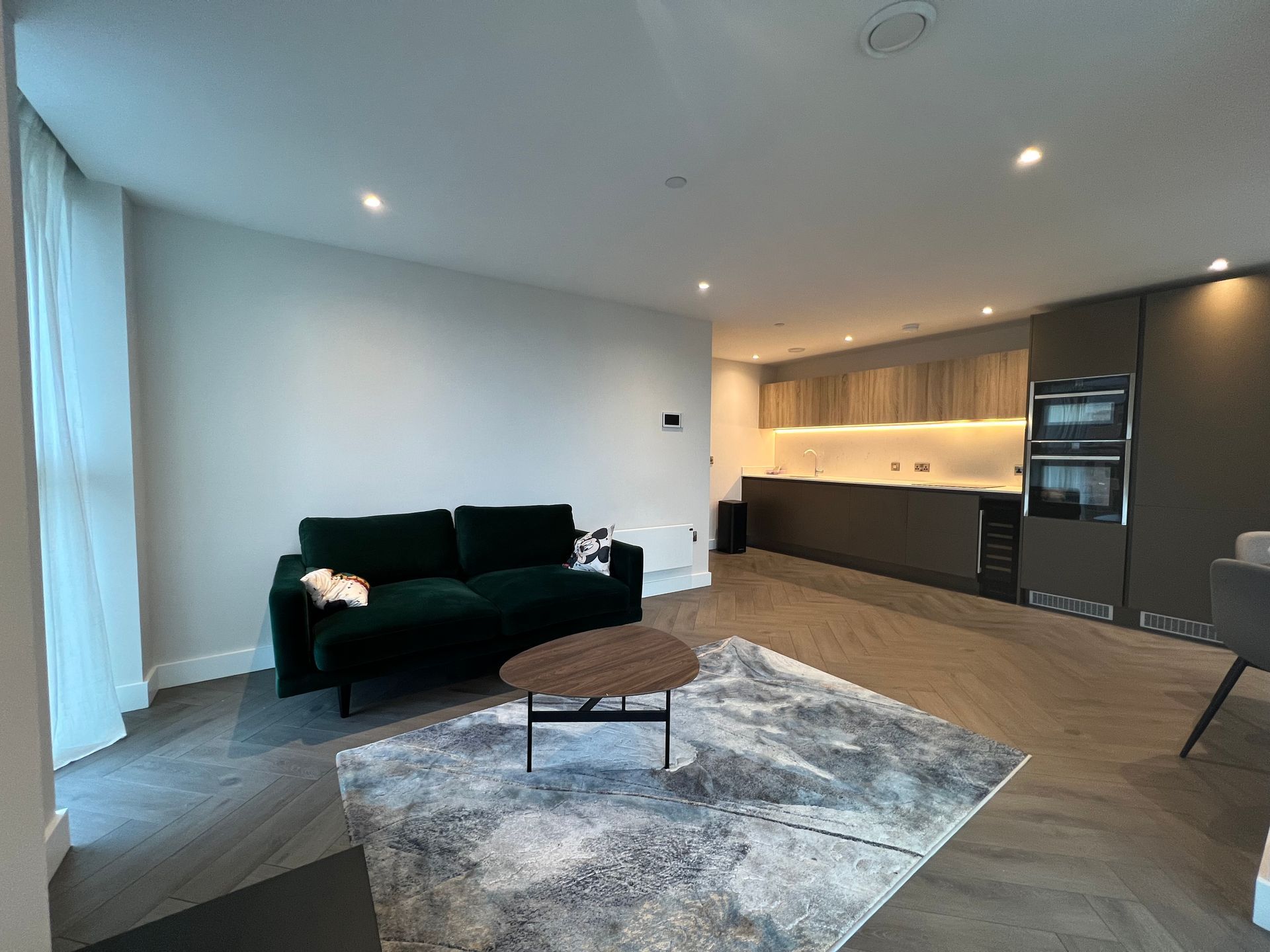 Modern apartment living room with green sofa, wooden coffee table, and kitchen in the background.
