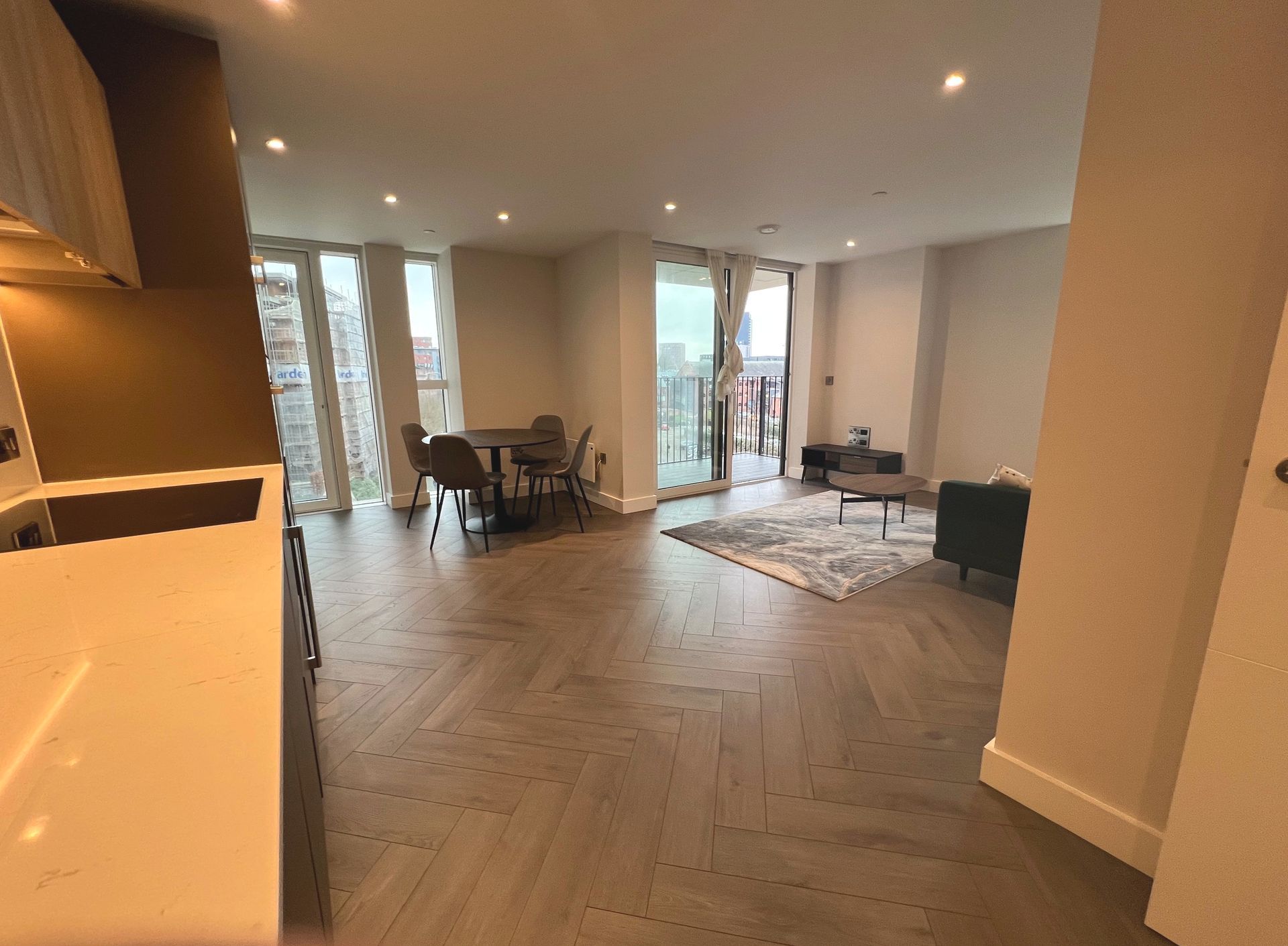 Spacious apartment with wood floors, dining table, sofa, and access to a balcony; neutral colors.