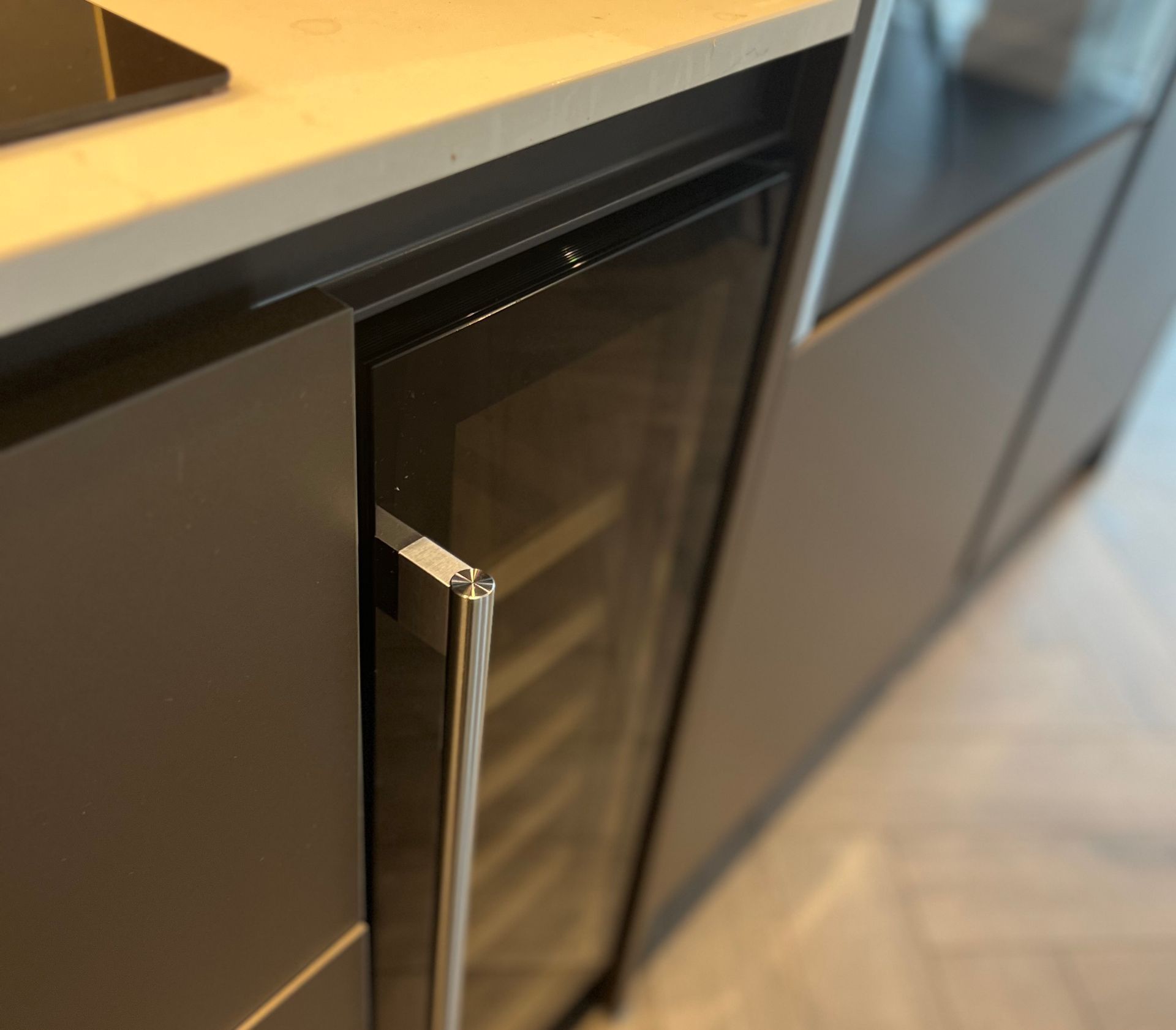 A built-in wine refrigerator with a glass door, open, set in dark gray cabinetry.