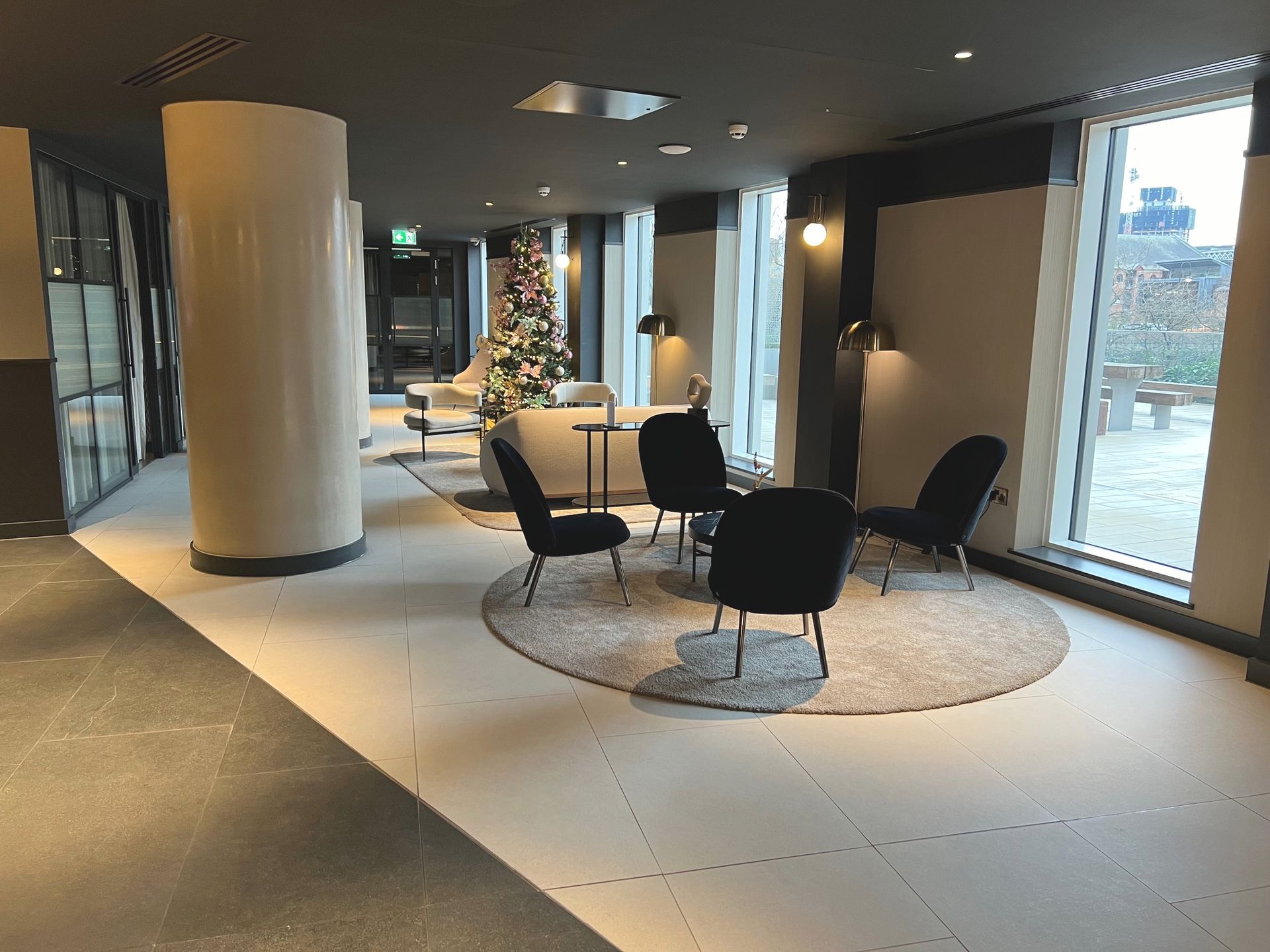 Modern lounge area with round rug, chairs, sofa, windows, and Christmas tree.