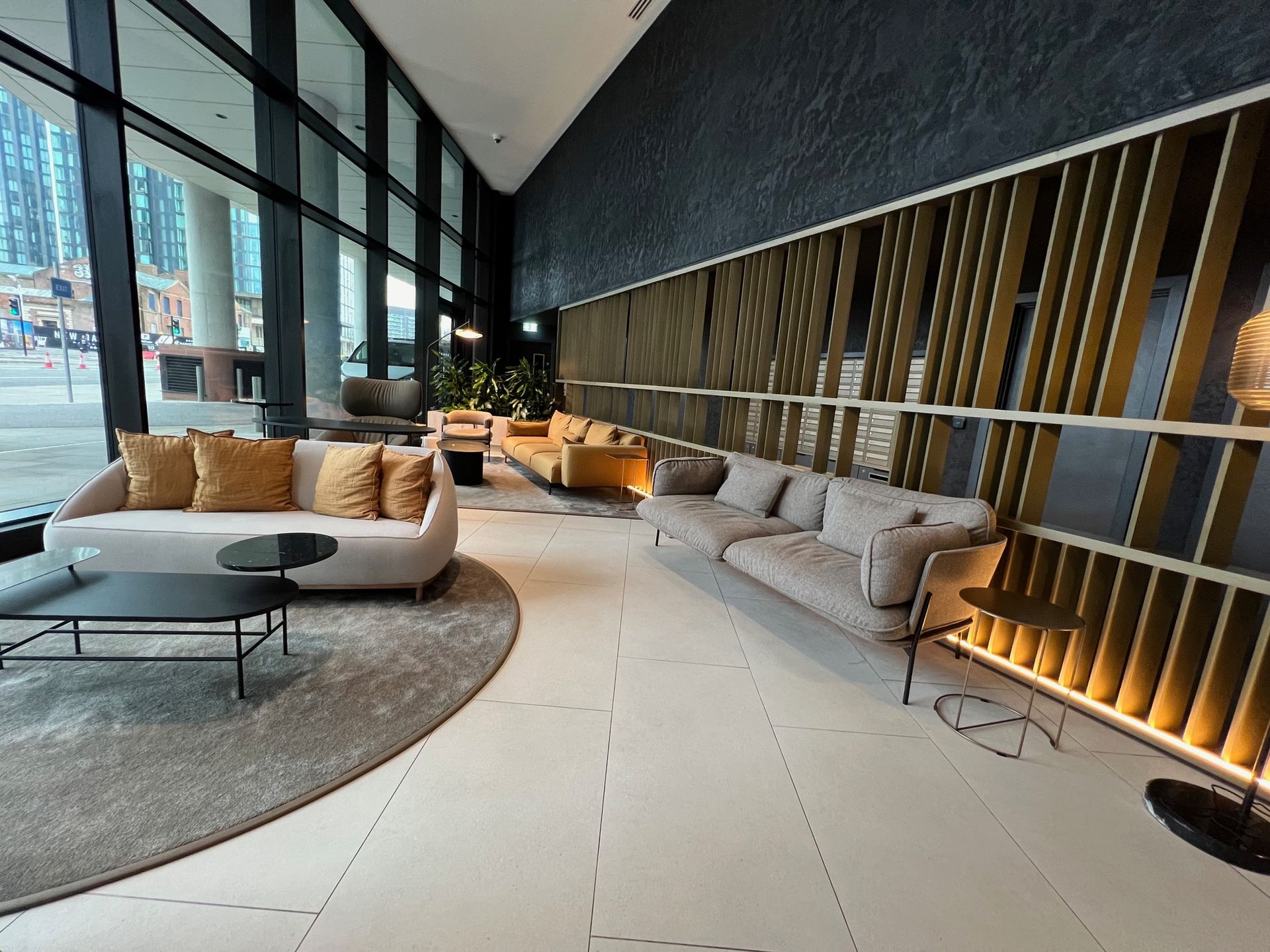 Lounge area with light-colored sofas, dark coffee tables, and gold accents. Large windows offer an outdoor view.