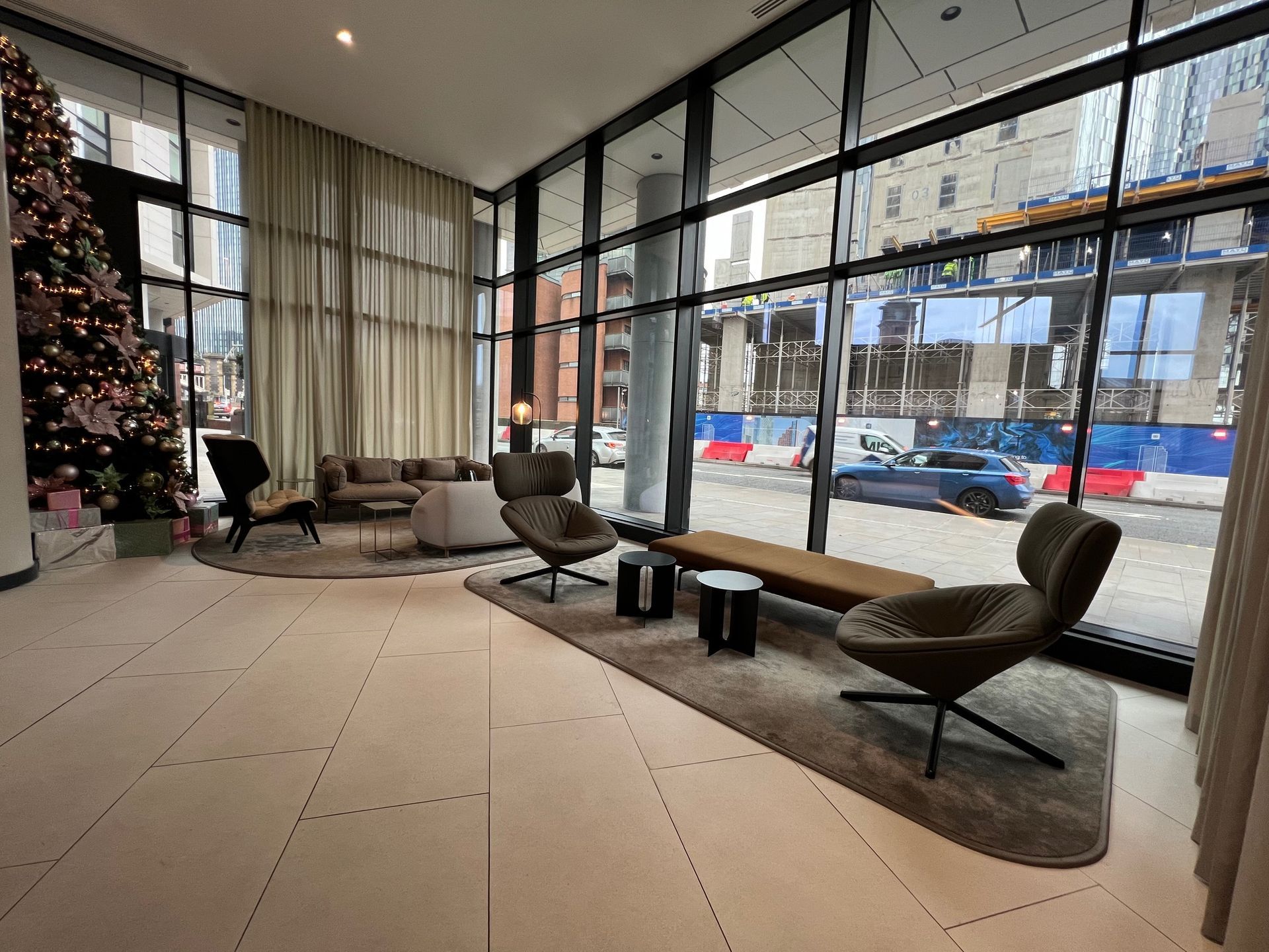 Modern lobby with seating, large windows, and Christmas tree. Street view visible outside.