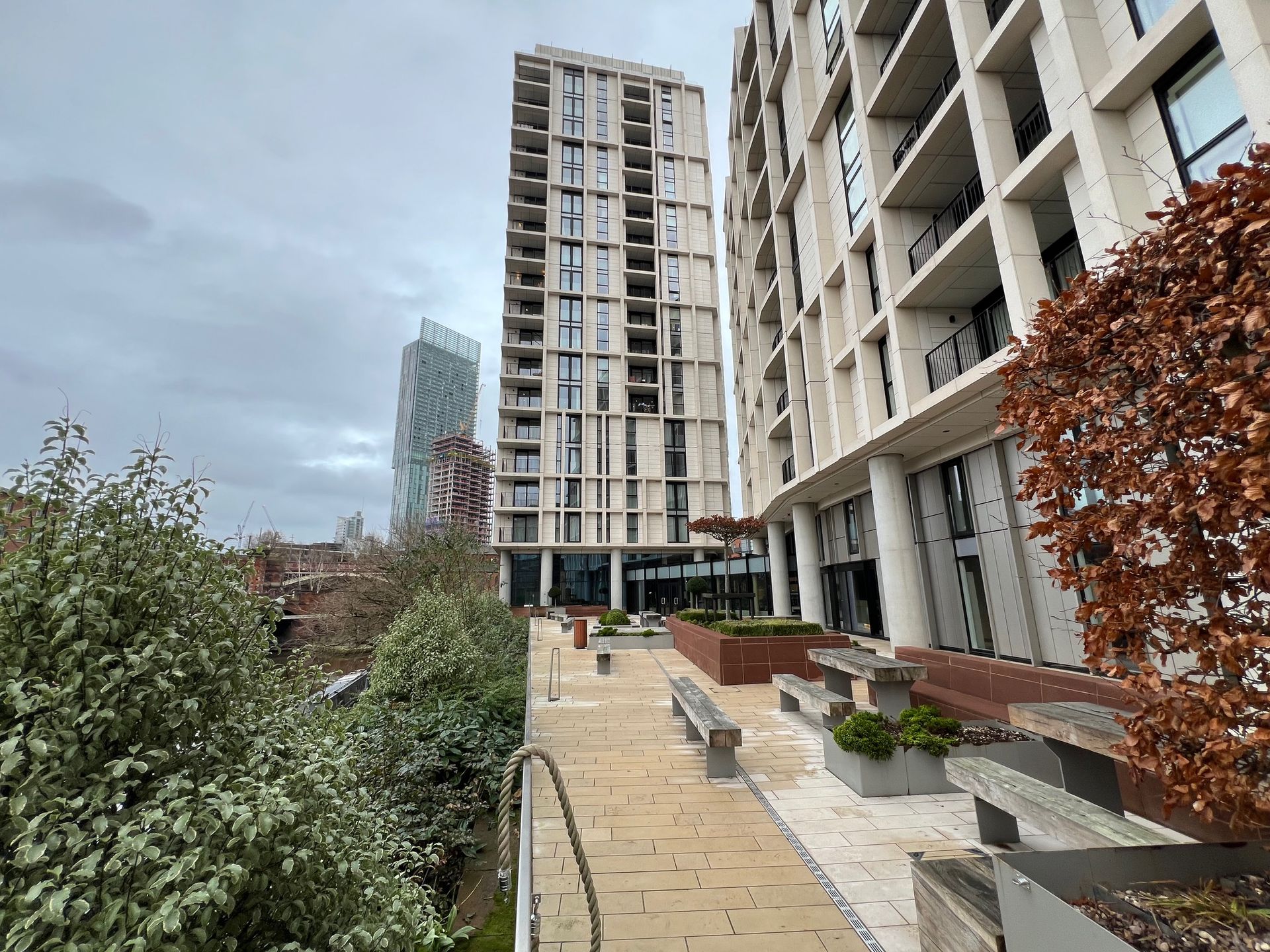 Modern apartment buildings with landscaped area and benches on an overcast day.