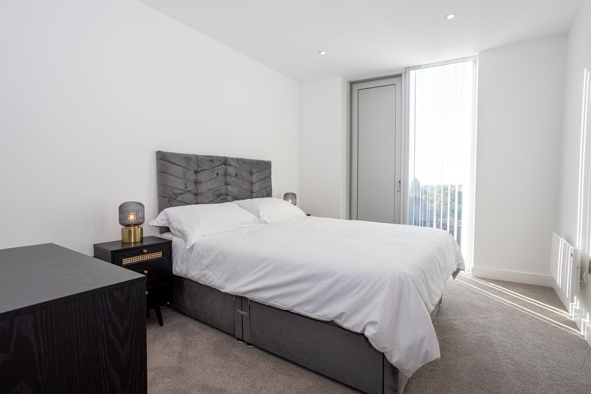 Bedroom with a gray bed, nightstand, and window with sheer curtains.