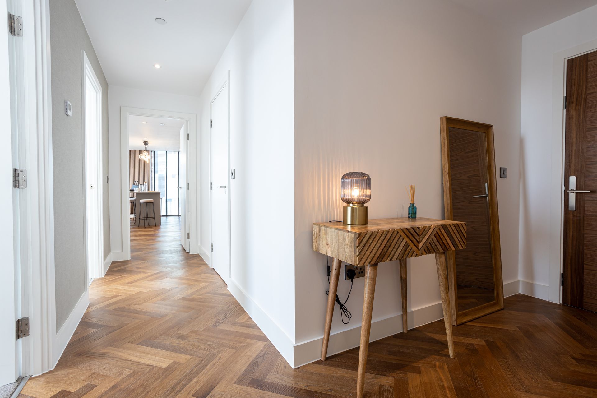 Hallway with herringbone wood floor, console table, mirror, and doorways.